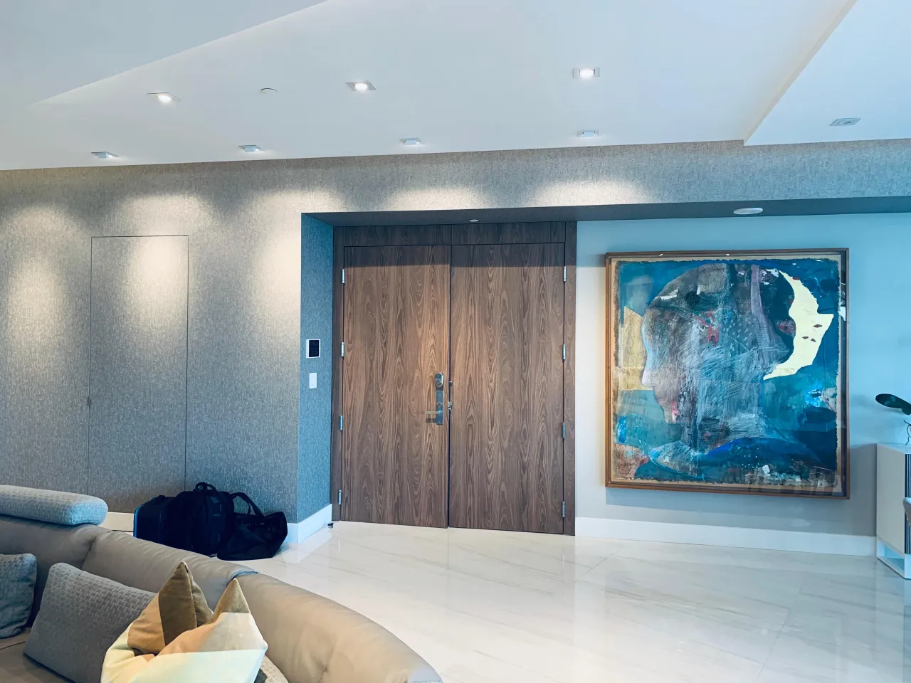 Wide wood-grain double door set in a gray textured wall with a concealed flush panel door alongside, polished light tile floor, framed artwork