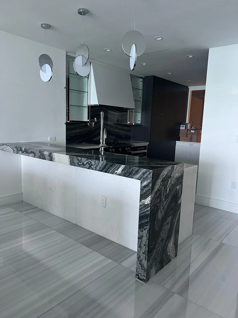 Black-and-white veined-stone waterfall kitchen island with modern disc pendant lights and a black cabinet/appliance wall