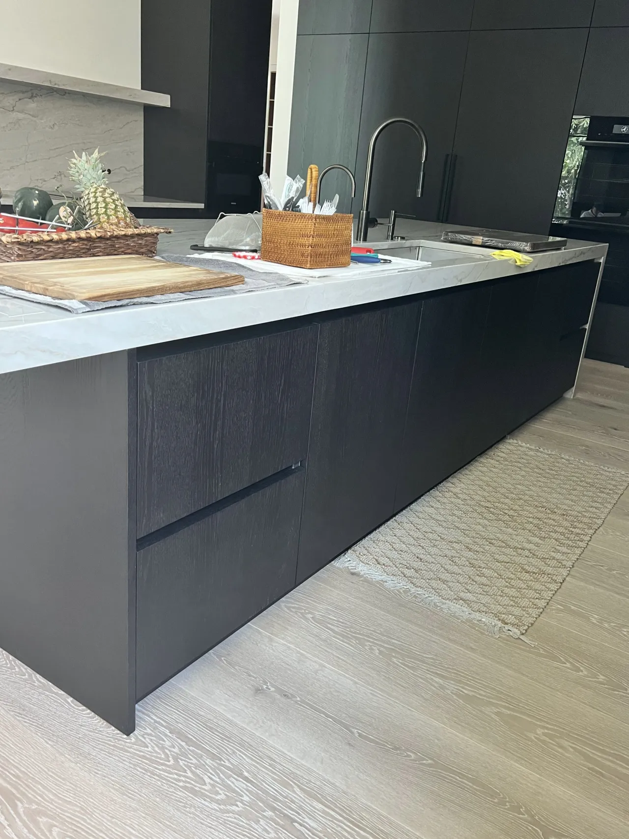 Black wood-grain kitchen island with a large drawer bank, a pull-down faucet, a stainless sink, and a veined-stone countertop