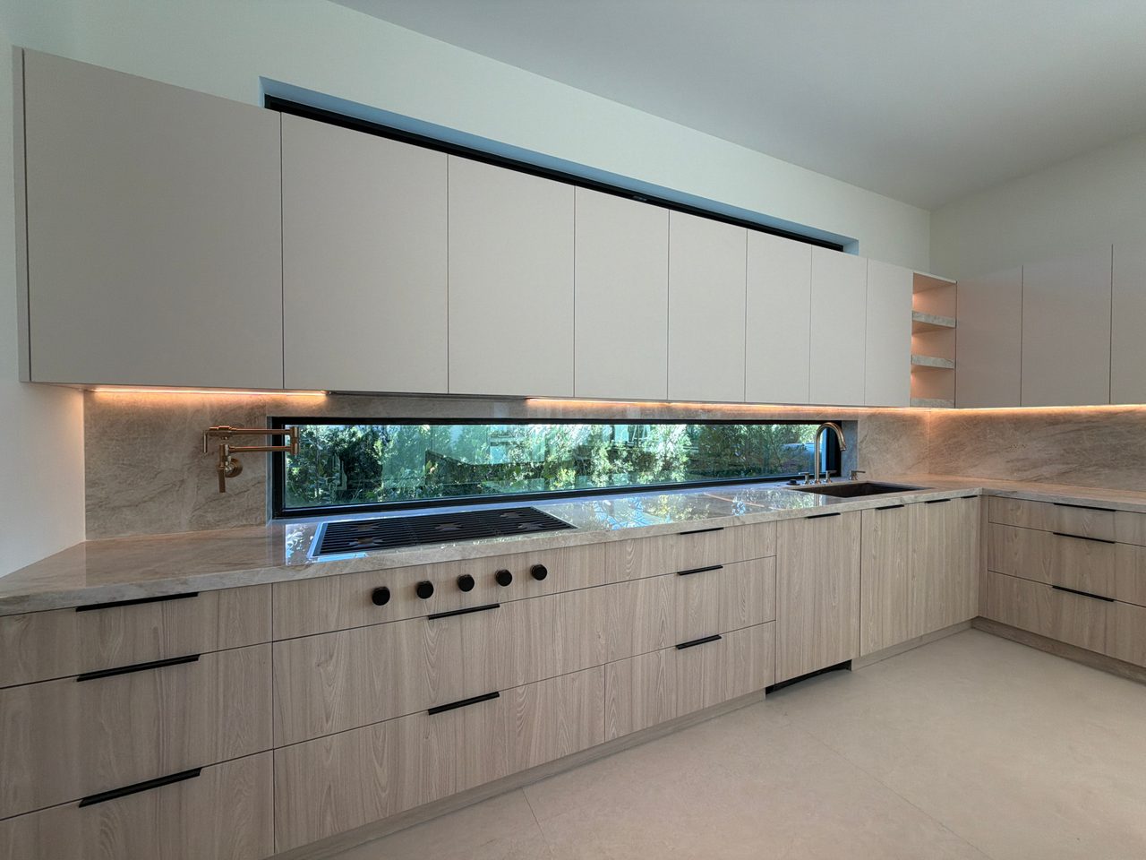Kitchen counter with white flat-panel upper cabinets, a veined-stone backsplash with a ribbon window, and light melamine lower cabinets with black pulls