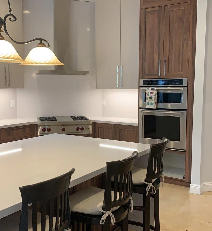 Kitchen with cream upper cabinets and dark wood-grain base cabinets, a white island with bar stools, a stainless rangetop, and stacked wall ovens
