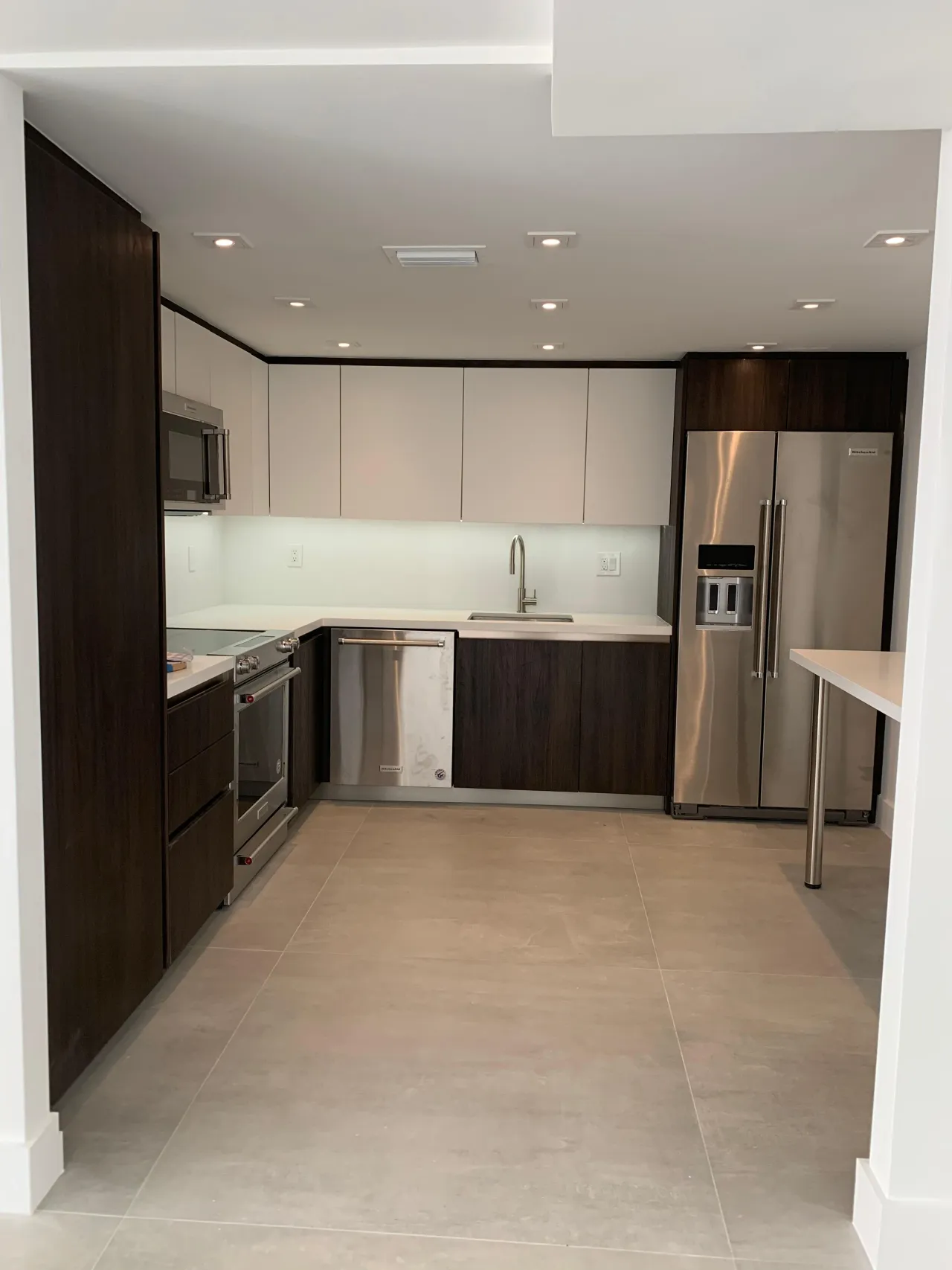 Dark brown/taupe U-shaped kitchen with stainless appliances, white countertops, and a light tile floor