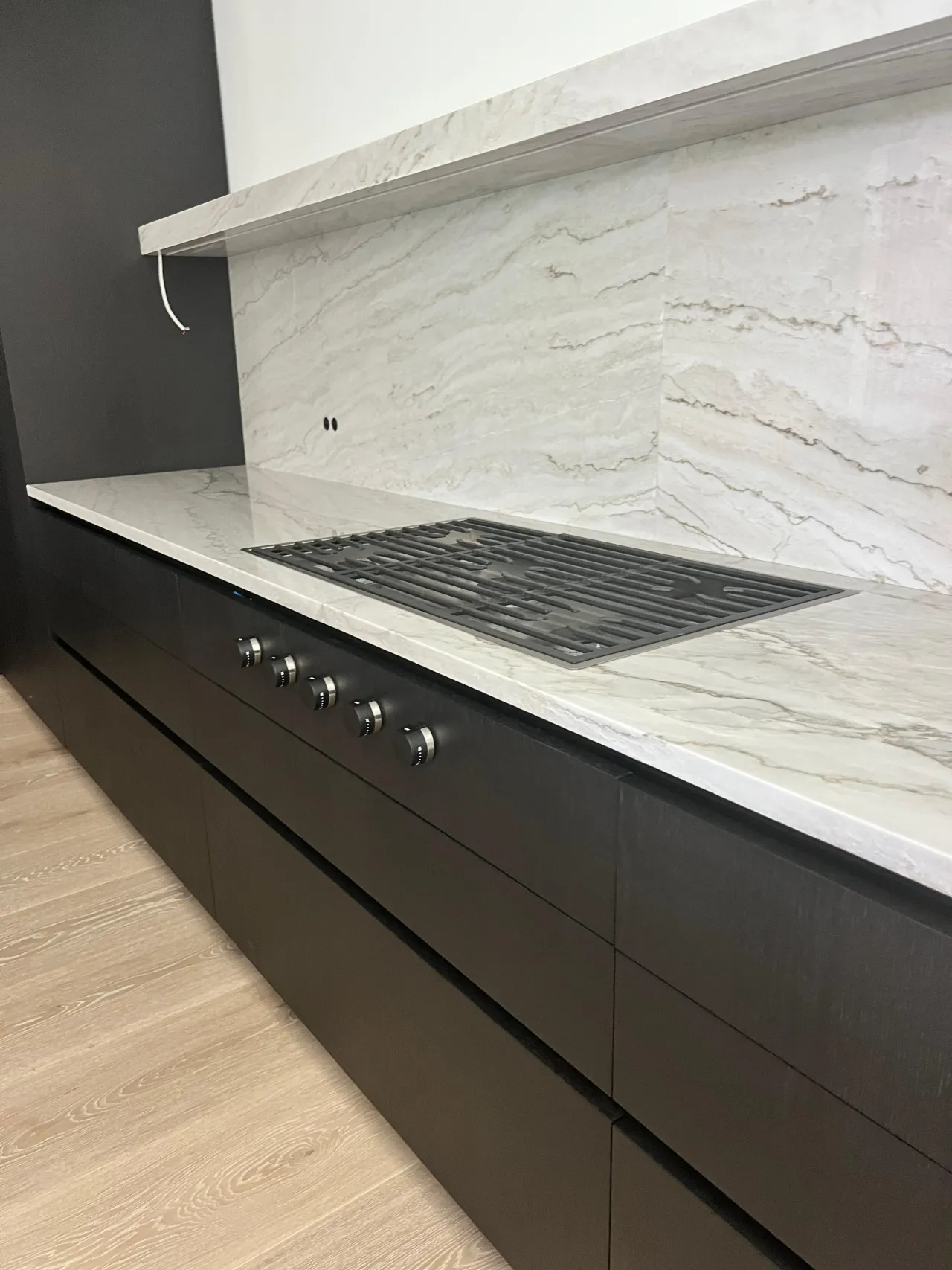 Dark cabinetry with a white/gray veined-stone countertop and matching backsplash, and a black gas cooktop set in the stone