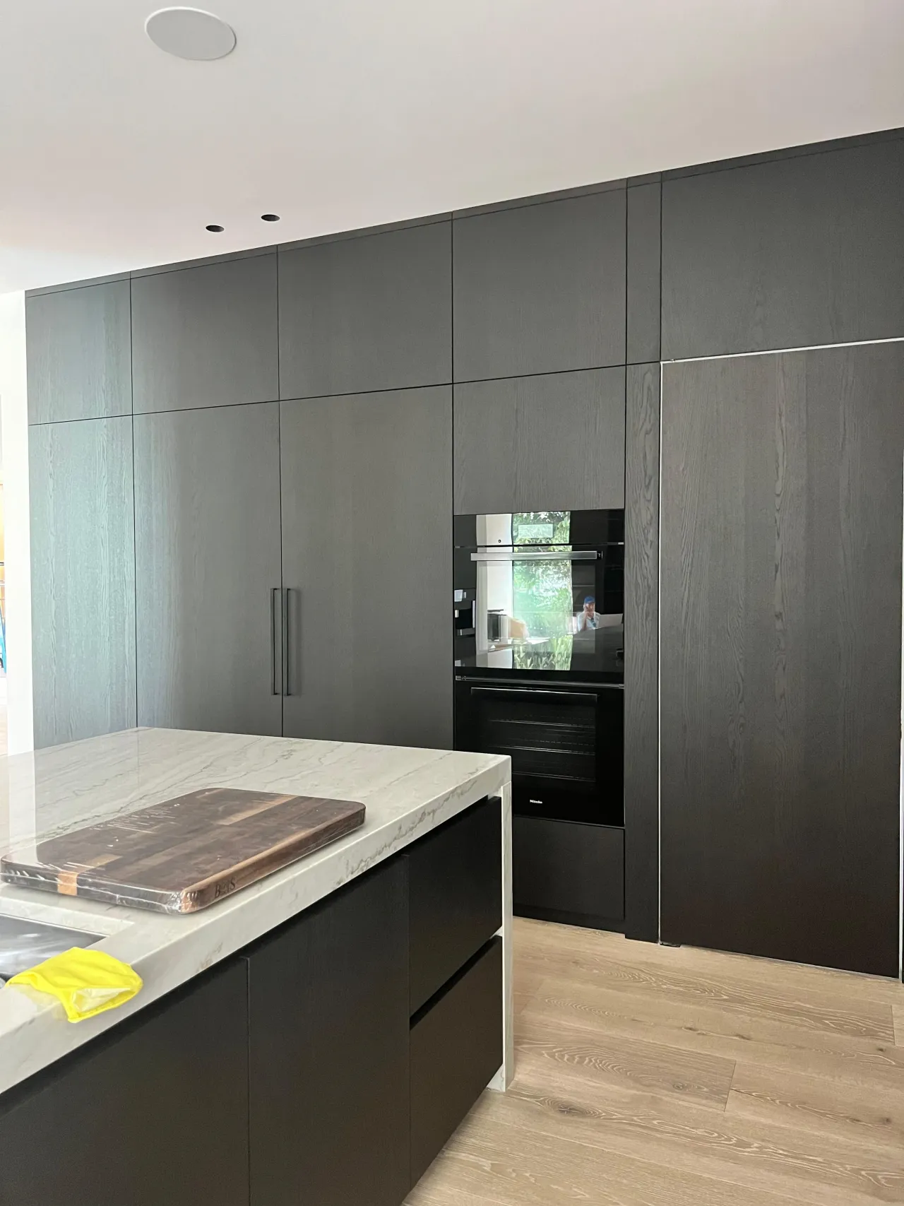 Dark charcoal floor-to-ceiling kitchen cabinets with an integrated black oven and a light stone waterfall island edge