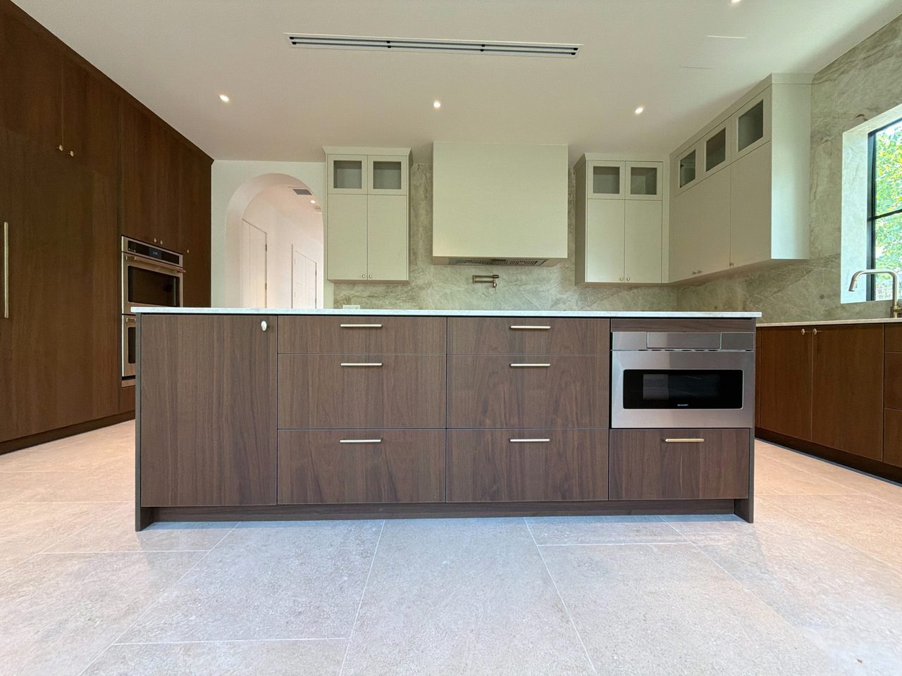Dark wood-grain melamine island with a bank of drawers, brushed-gold bar pulls, a veined-stone top, and a built-in stainless microwave drawer