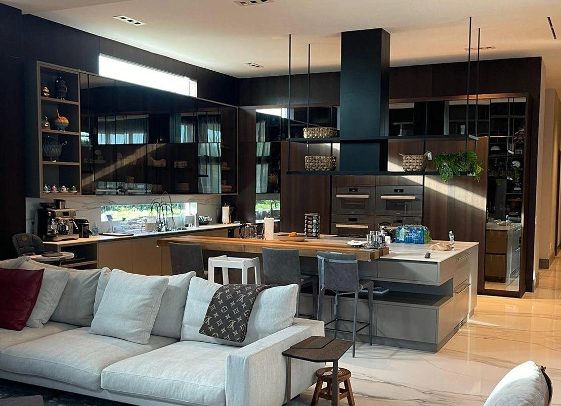 Dark open-concept kitchen with a wood breakfast bar, glass-front display cabinets, and a hanging pendant light
