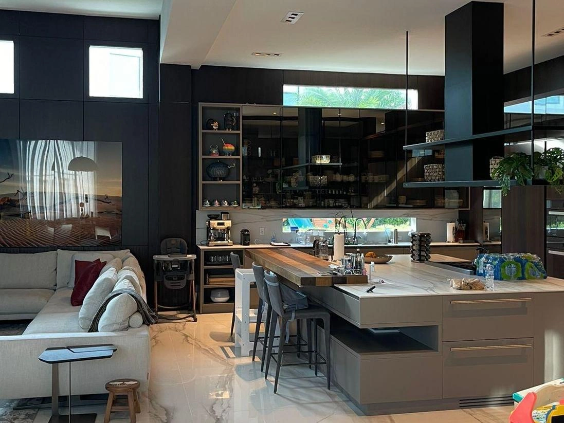 Dark open kitchen with a stone floor, a breakfast bar with a wood counter, a glass window backsplash, and a living area beyond
