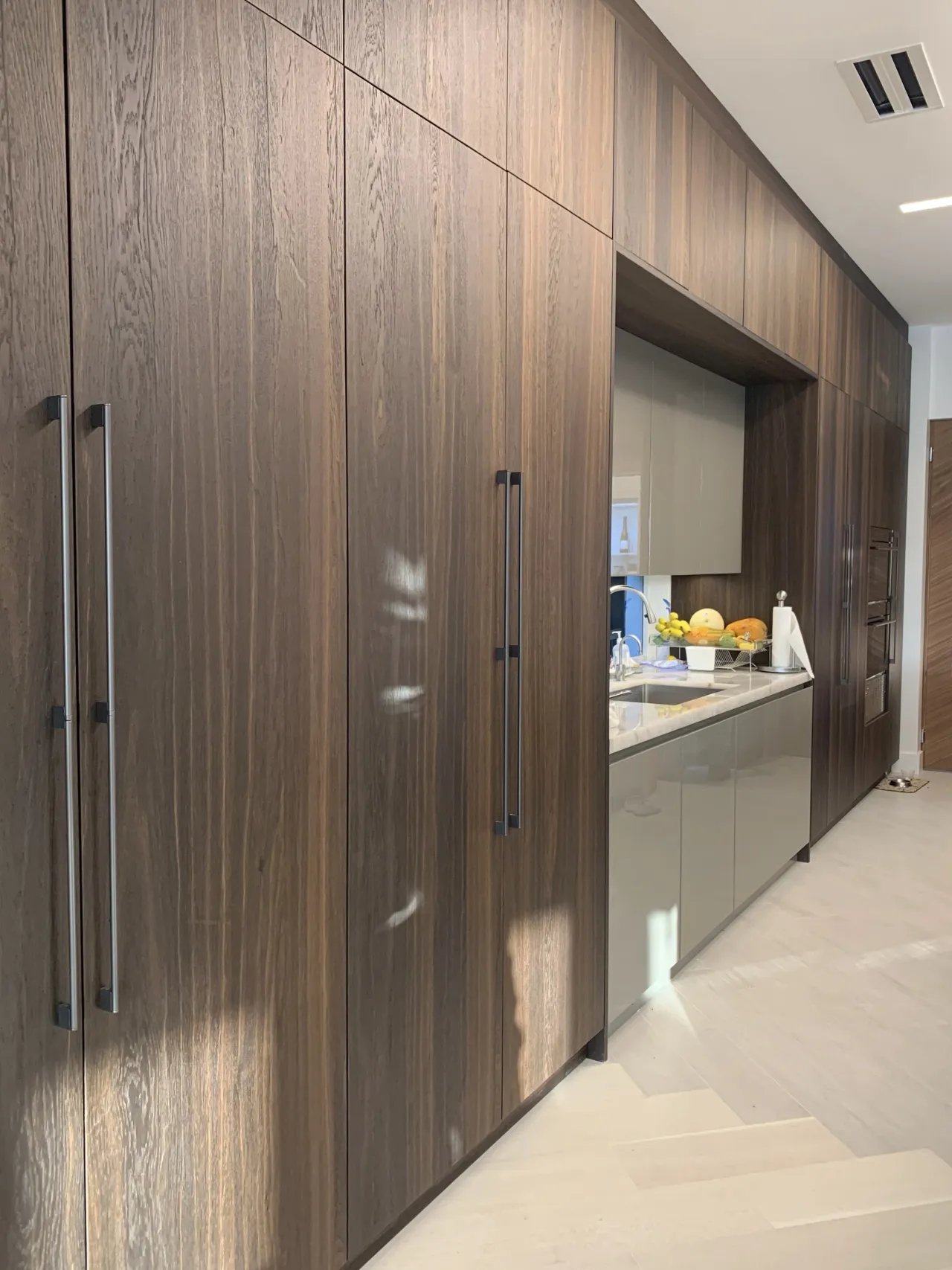 Dark wood floor-to-ceiling cabinetry wall with integrated paneled refrigerator/freezer columns and long stainless bar-pull handles
