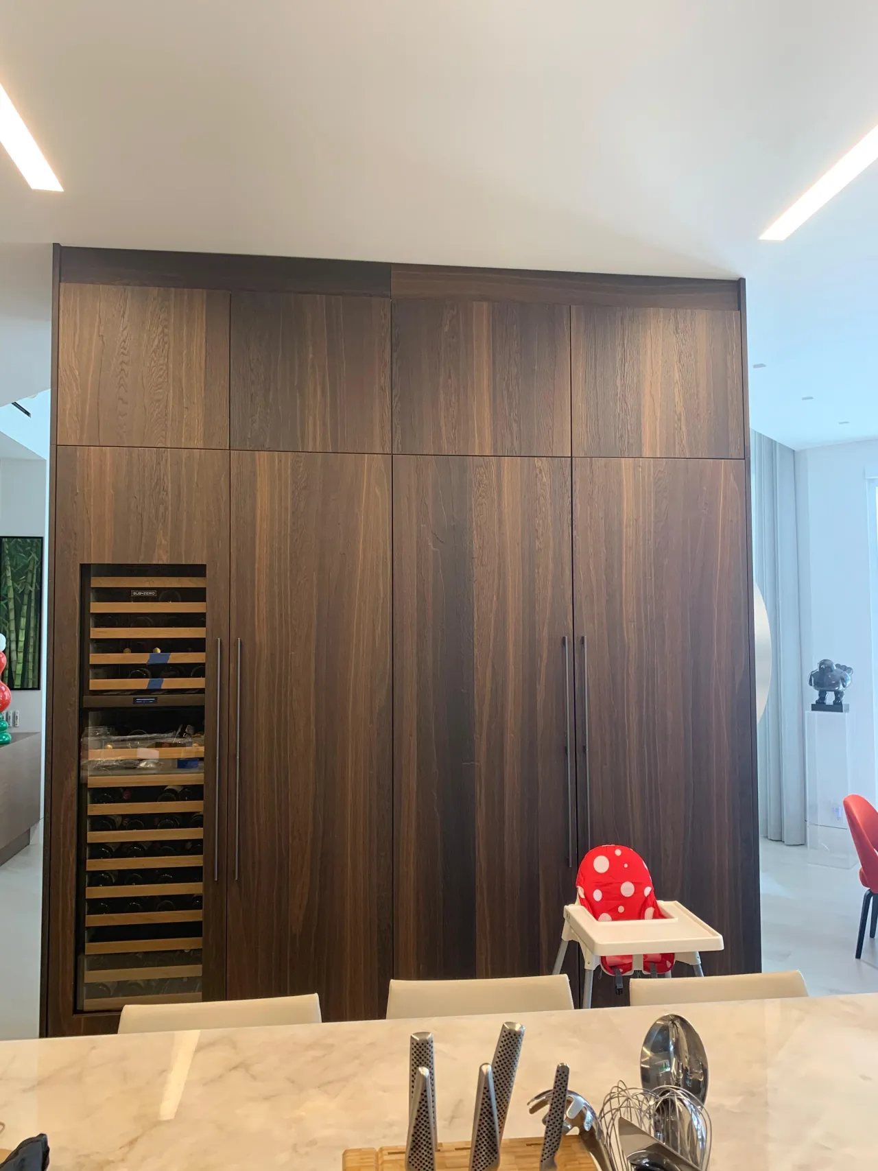 Dark wood floor-to-ceiling pantry wall with a built-in glass-front wine column and tall panel doors with thin bar pulls