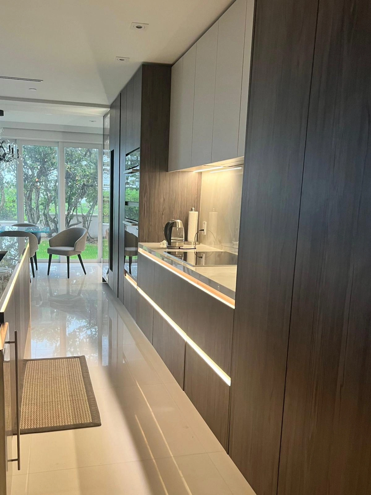 Dark wood galley kitchen with LED under-cabinet strip lighting, a glass cooktop, and a light gray polished tile floor