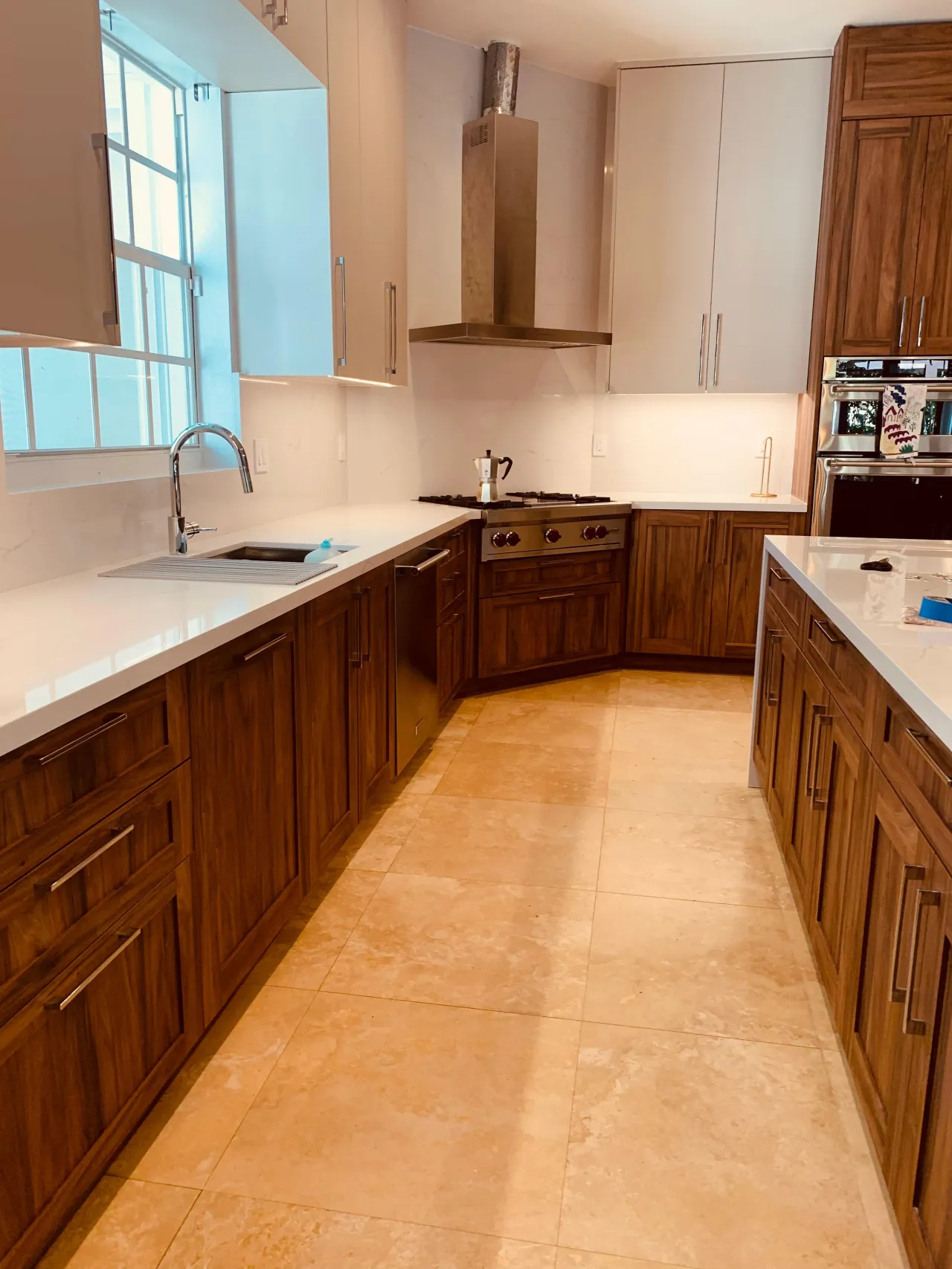 Dark wood-grain cabinets with white stone counters, a stainless range under a stainless hood, a dishwasher, double wall ovens and a stone tile floor