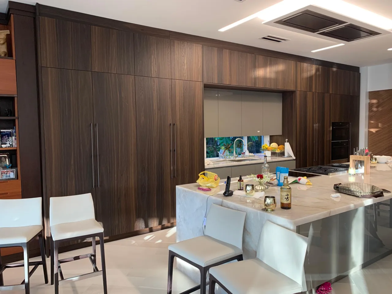Dark wood-grain floor-to-ceiling cabinets with a veined-stone waterfall island bar seating area and bottles and decor on the counter