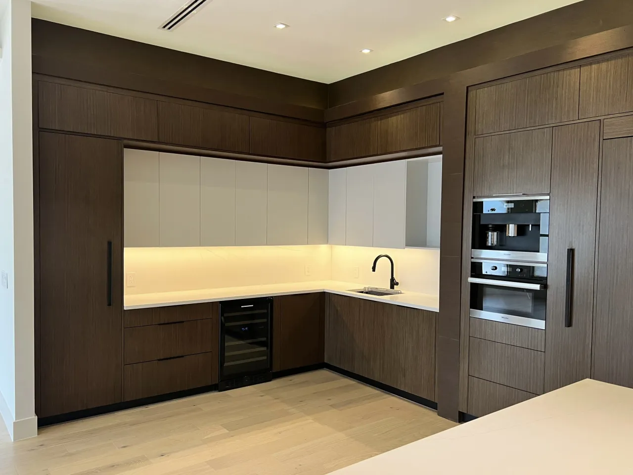 Dark wood-grain kitchen cabinets with a light stone counter, a built-in coffee machine and wall oven with a warming drawer, and LED under-cabinet lighting