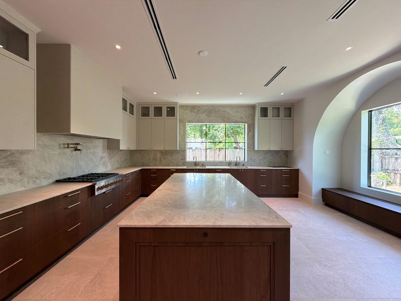 Dark wood-grain melamine kitchen with a long veined-stone waterfall island, cream upper cabinets, a gas rangetop, and a built-in window bench
