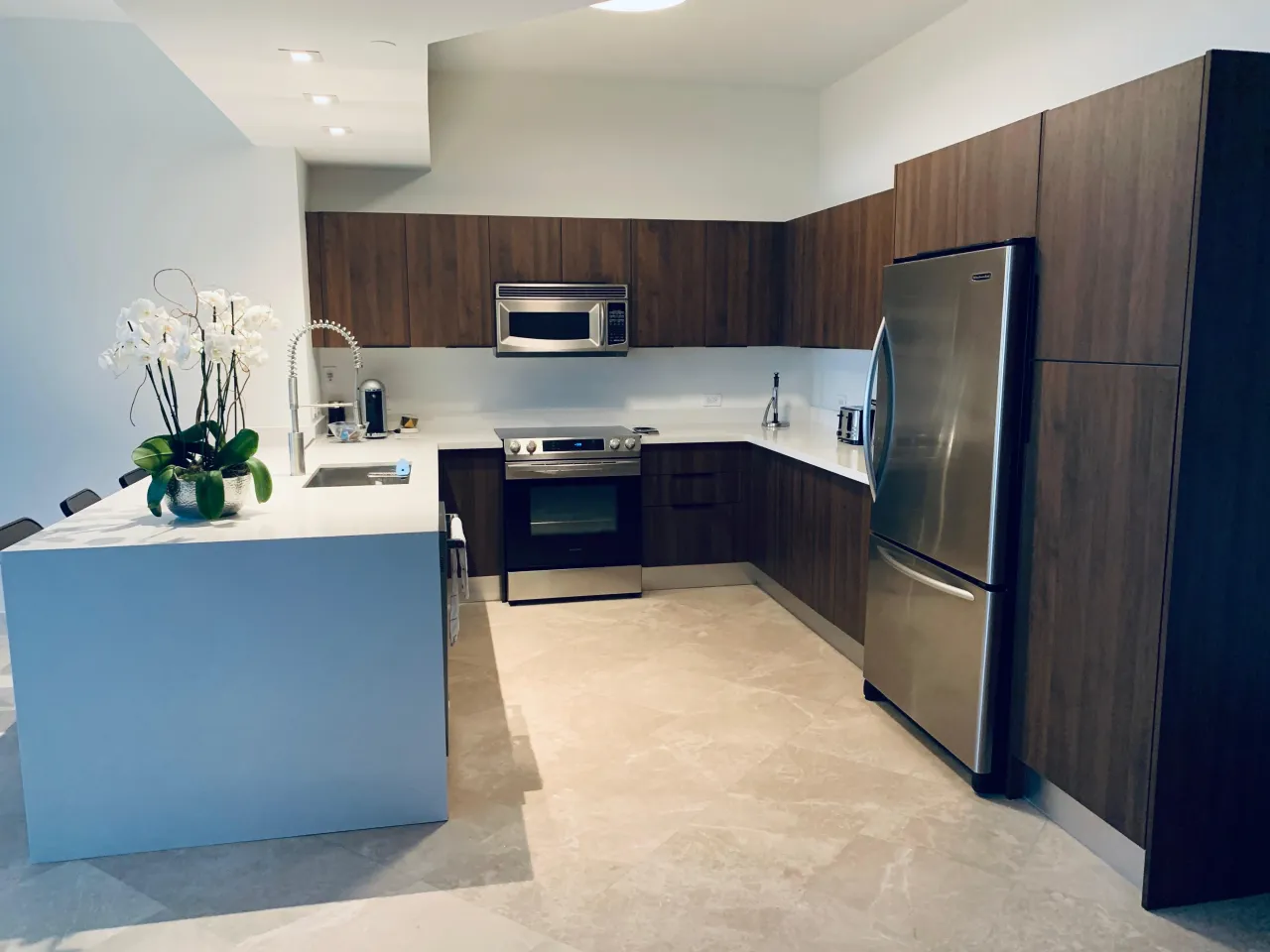 Dark wood kitchen with a white waterfall peninsula, black barstools, and an orchid arrangement on the counter