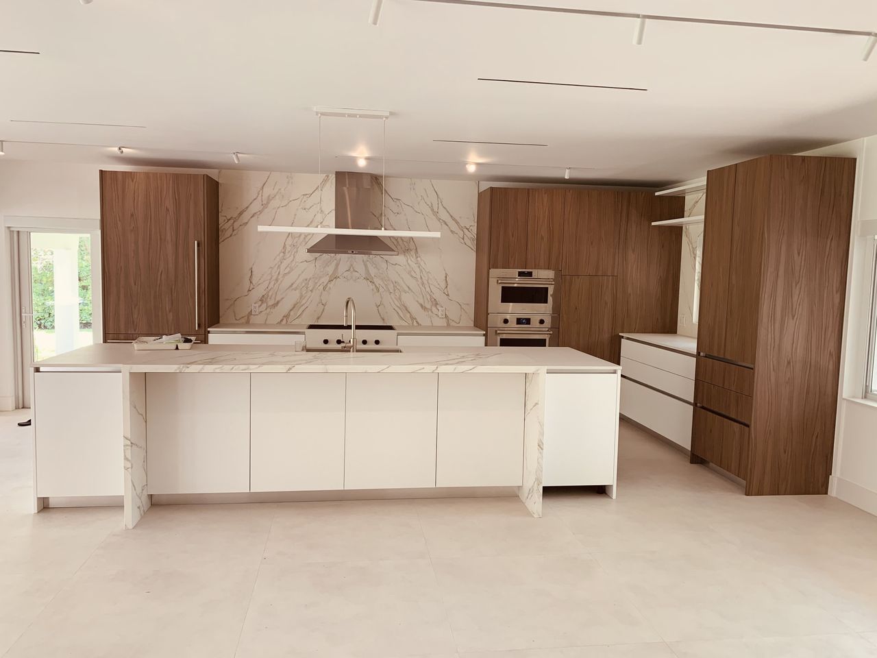 Kitchen with dark wood tall cabinets, a stainless double wall oven, and a veined-stone backsplash