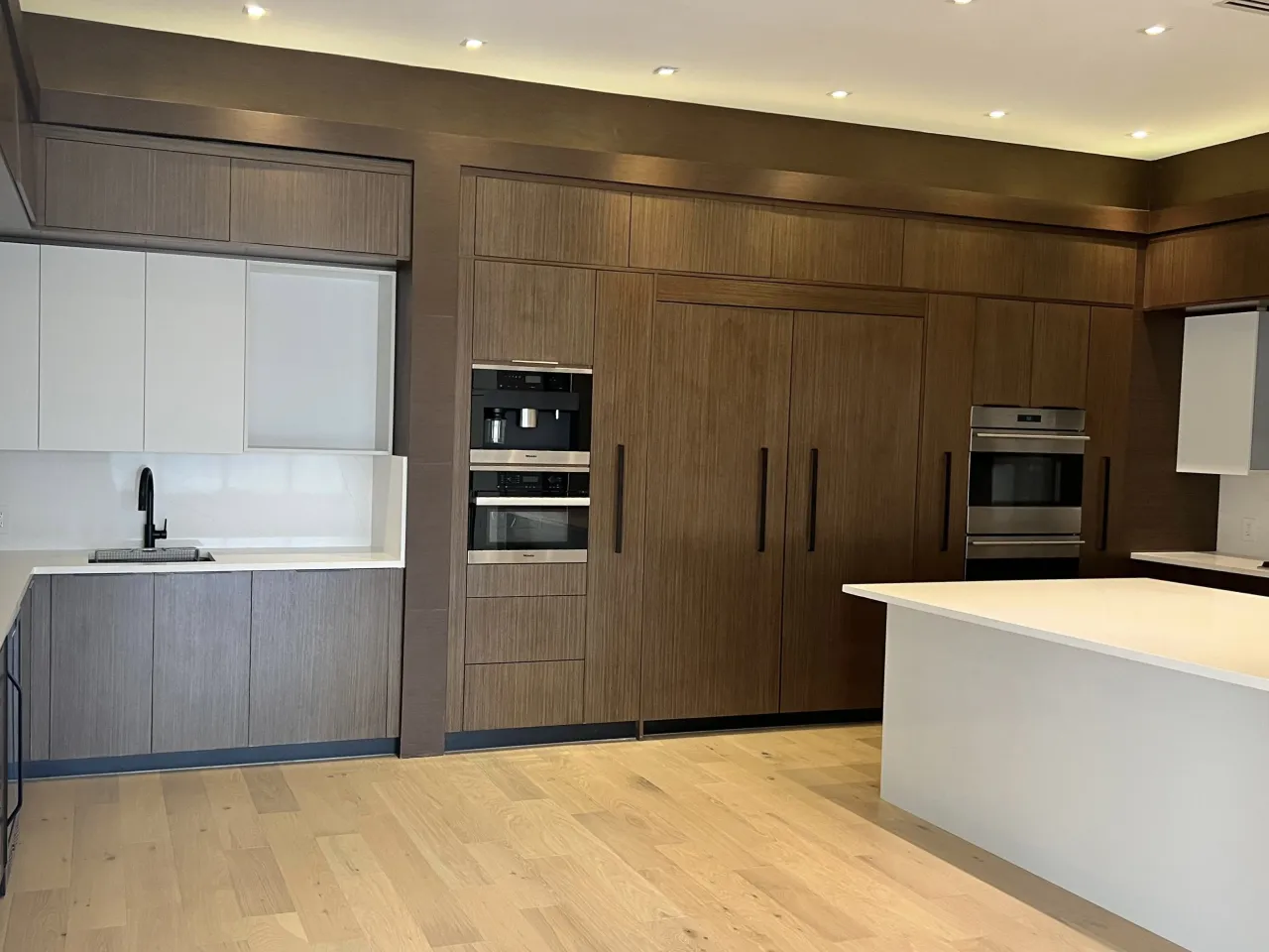 Dark wood and white L-shaped kitchen with a built-in wall coffee/oven column and light hardwood flooring