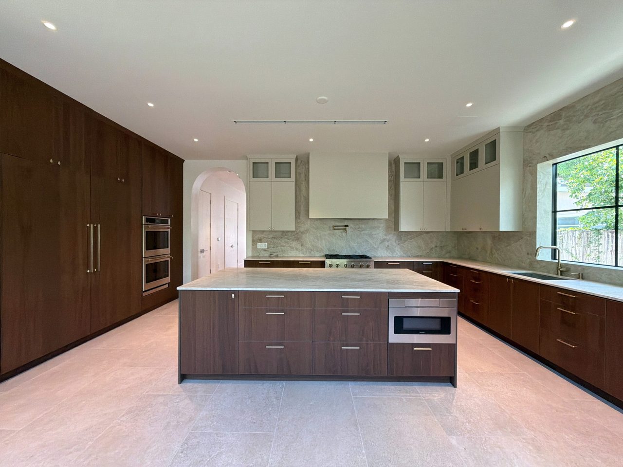 Floor-to-ceiling dark melamine cabinetry with a stainless double wall oven and panel-front refrigerator, beside an island with a microwave drawer