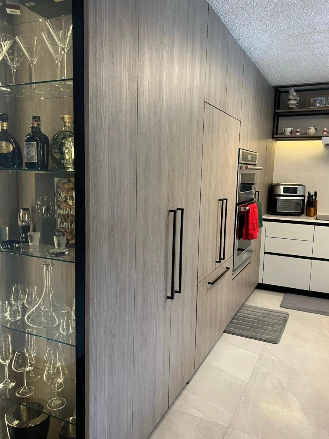 Floor-to-ceiling gray wood-grain pantry wall with black hardware pulls and an illuminated shelf niche above