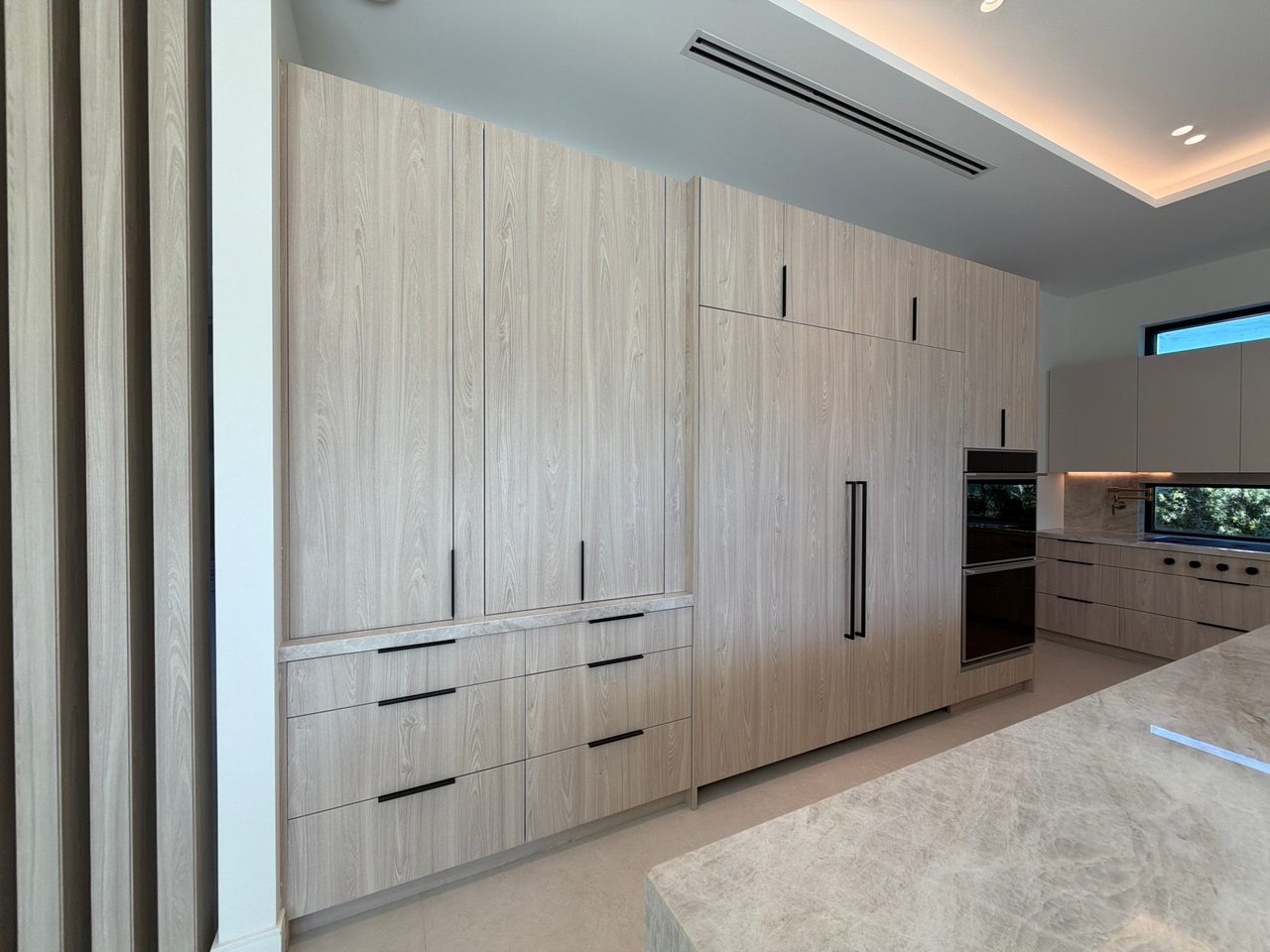 Floor-to-ceiling light melamine pantry and cabinet wall with black bar pulls, an integrated paneled refrigerator, and a stainless double wall oven