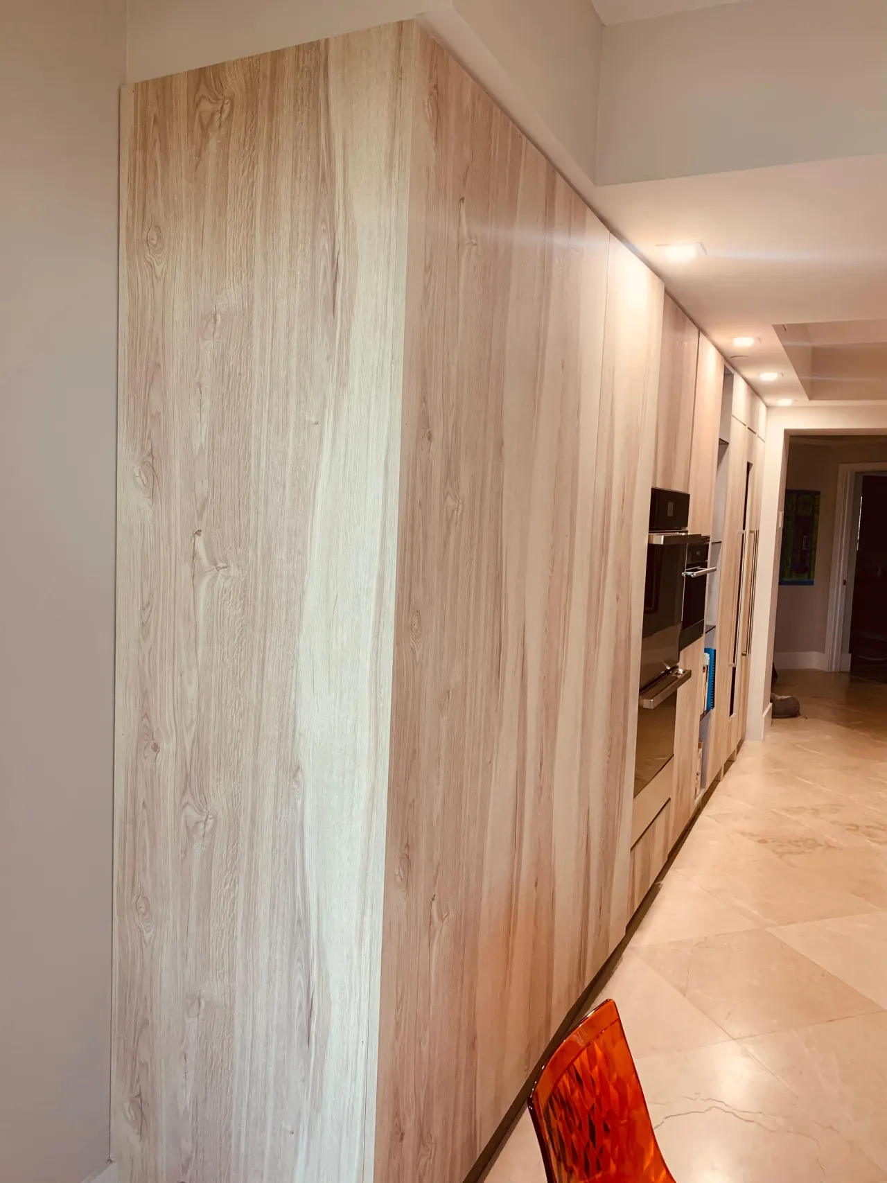 Floor-to-ceiling light wood-grain pantry wall with integrated stainless double ovens and wall storage, tile floor