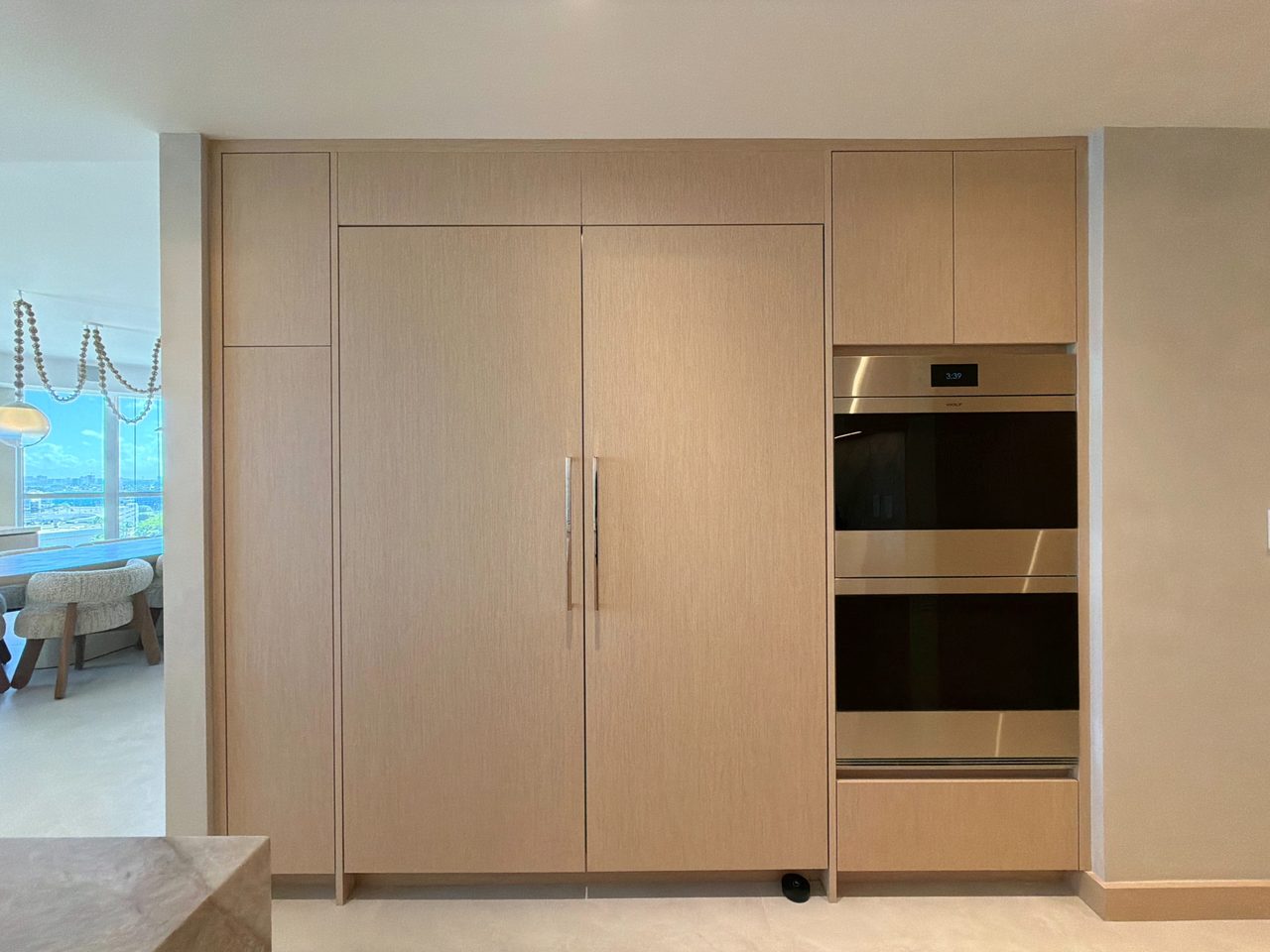 Floor-to-ceiling pale custom-stained wood veneer wall with a panel-front refrigerator, a stainless double wall oven, and full-height cabinets