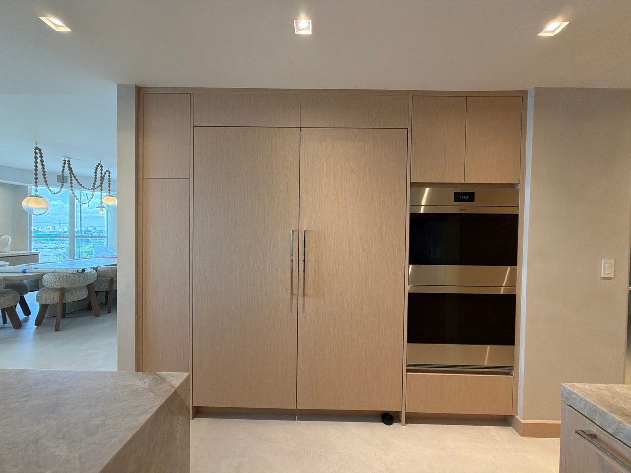 Full-height custom-stained wood veneer cabinet wall with paneled refrigerator doors, chrome pulls, and a built-in stainless double wall oven