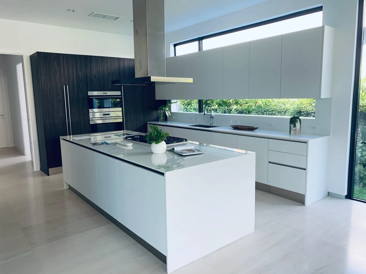 Modern kitchen with a glass cooktop island, a glass countertop, a full window wall for natural light, and minimalist white cabinets