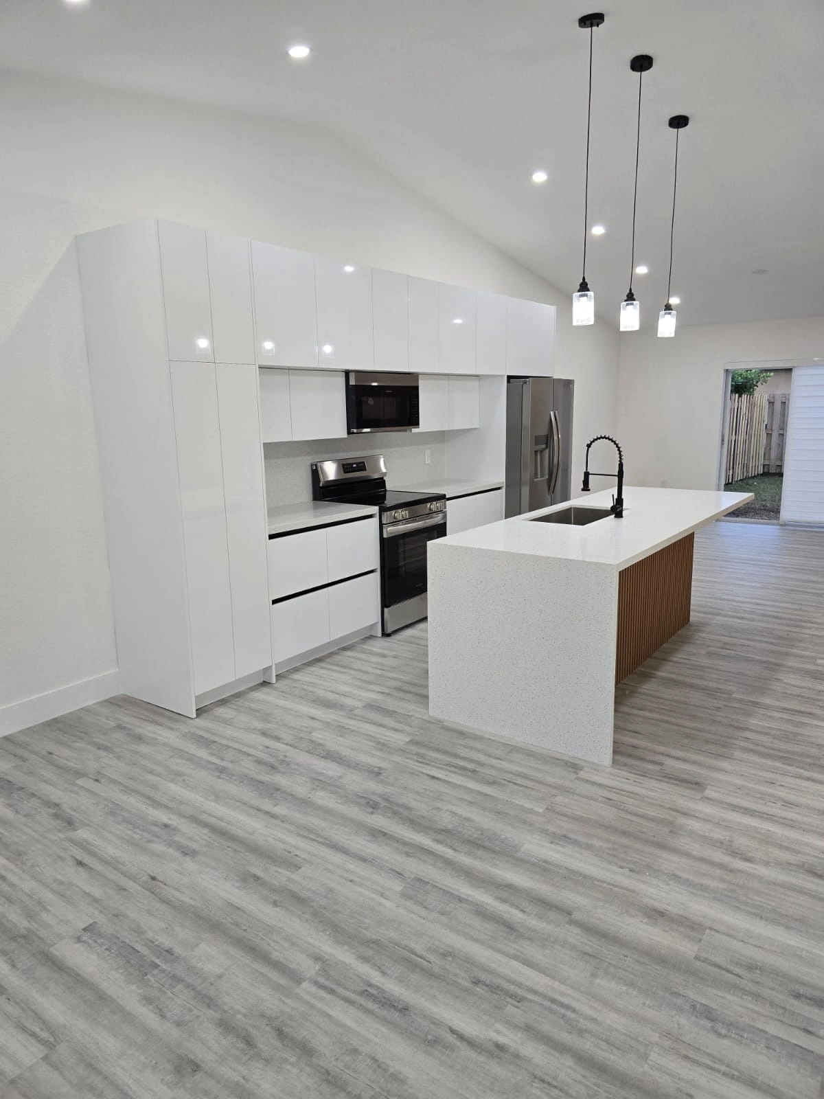 High-gloss white kitchen with a stainless range and over-range microwave, plus an island with a white stone top and a slatted wood front