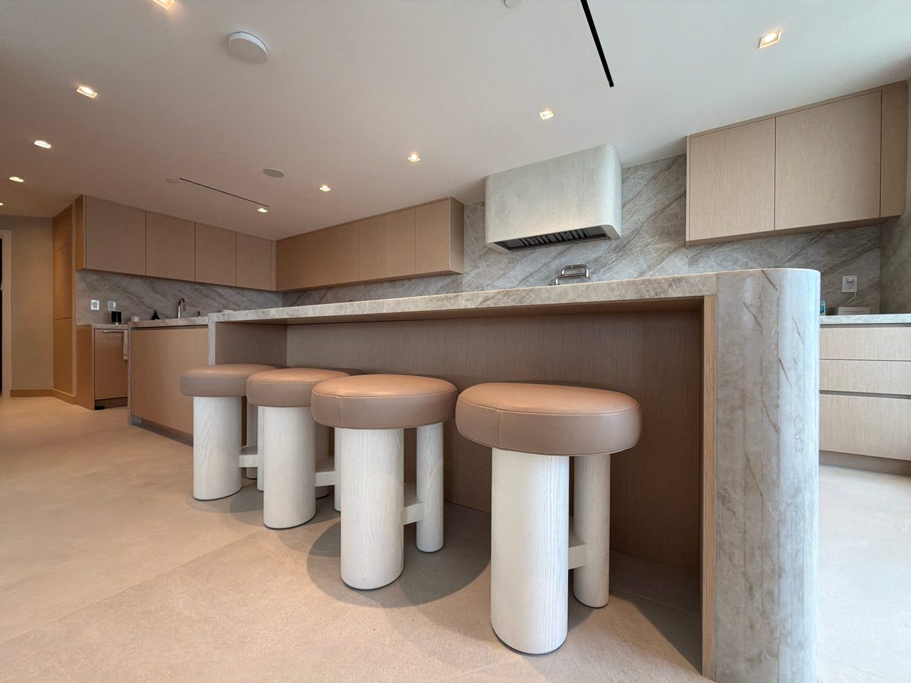 Island bar with a veined-stone top and rounded corner, custom-stained wood veneer panel back, and four cream stools with leather seats