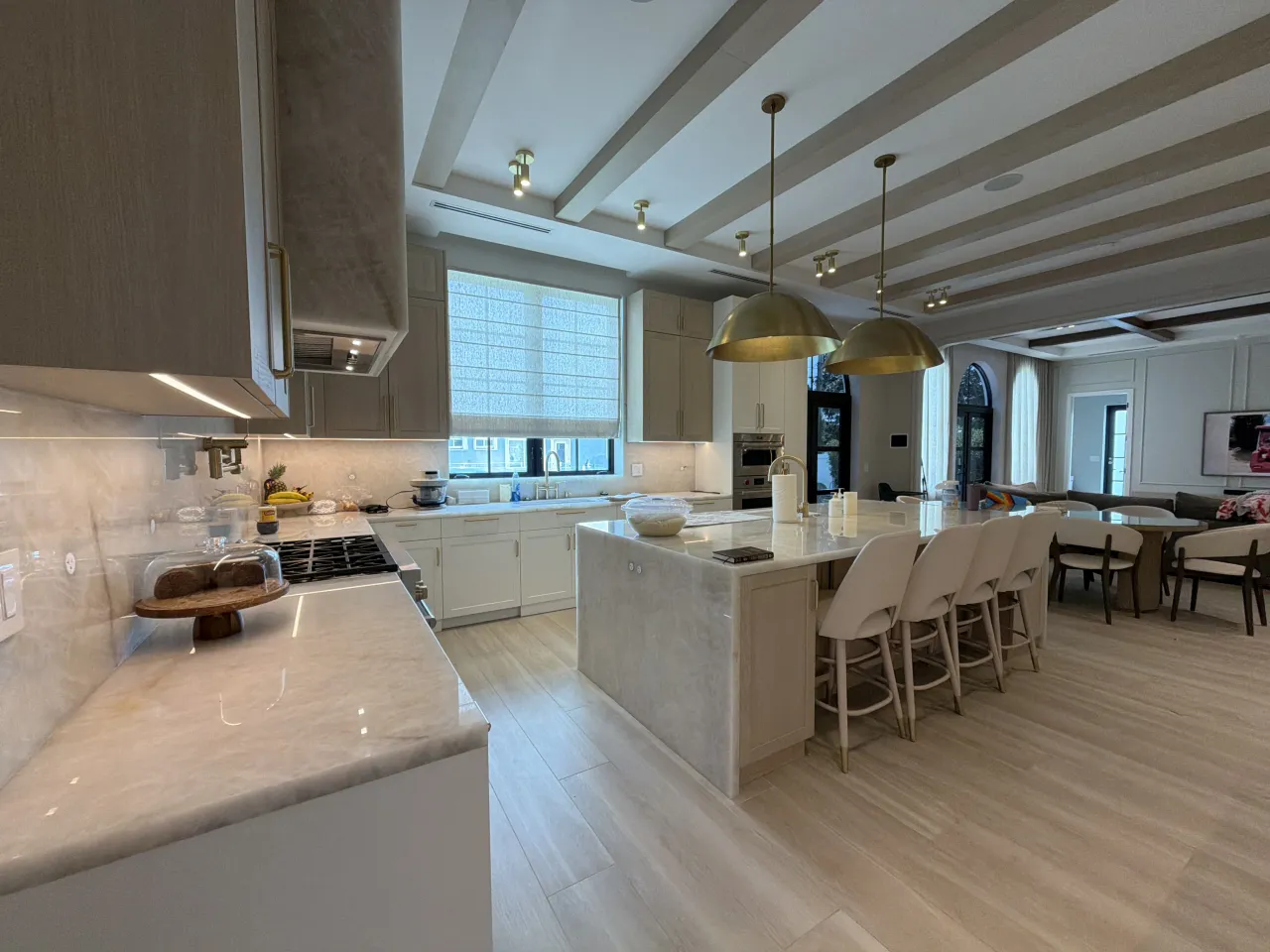 Kitchen island with a white veined-stone waterfall countertop and gold-tone dome pendants, opening into a connected dining and living area