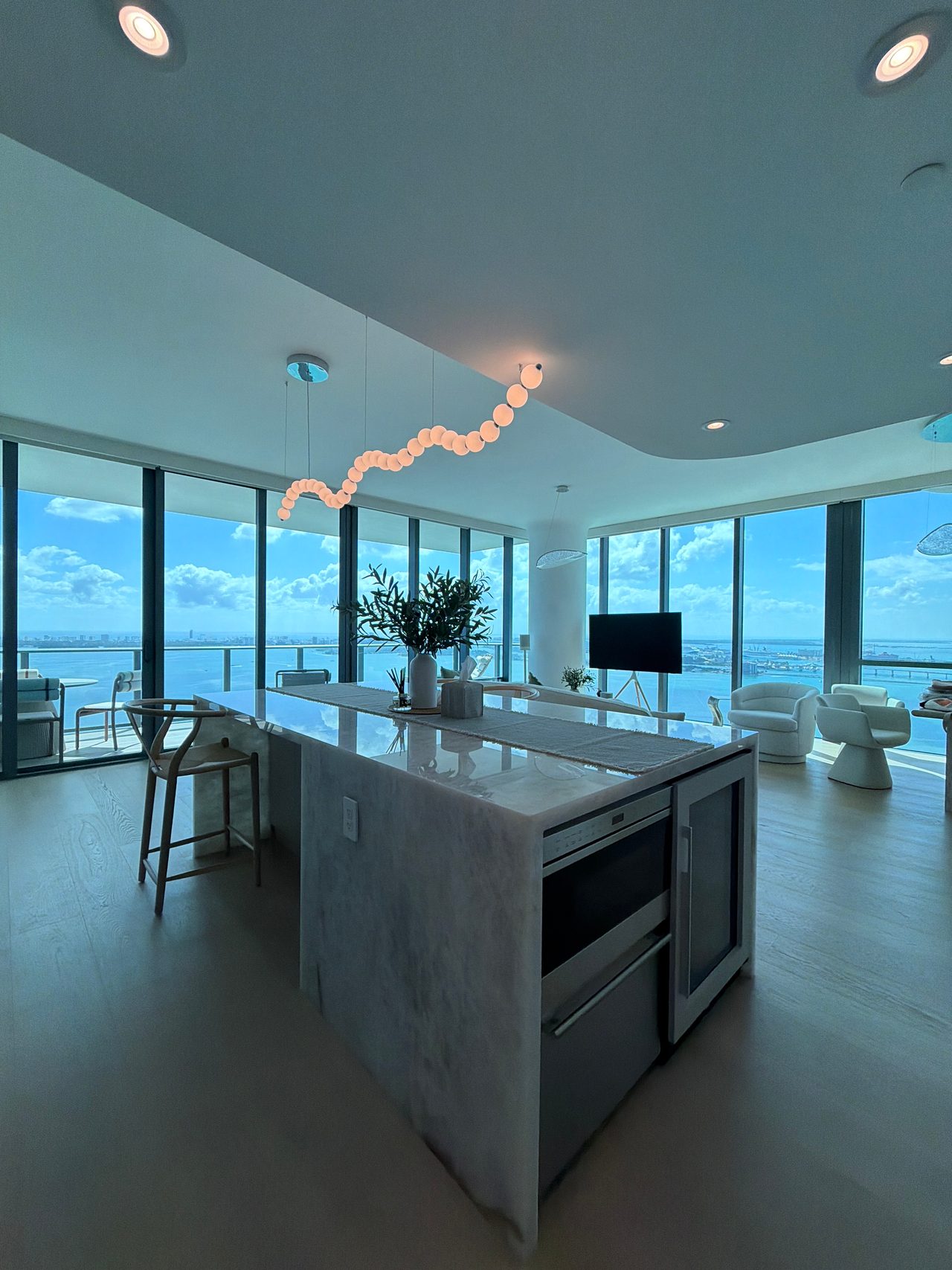 Kitchen island with a wine cooler and veined-stone top, wood barstools, and ocean-view windows beyond
