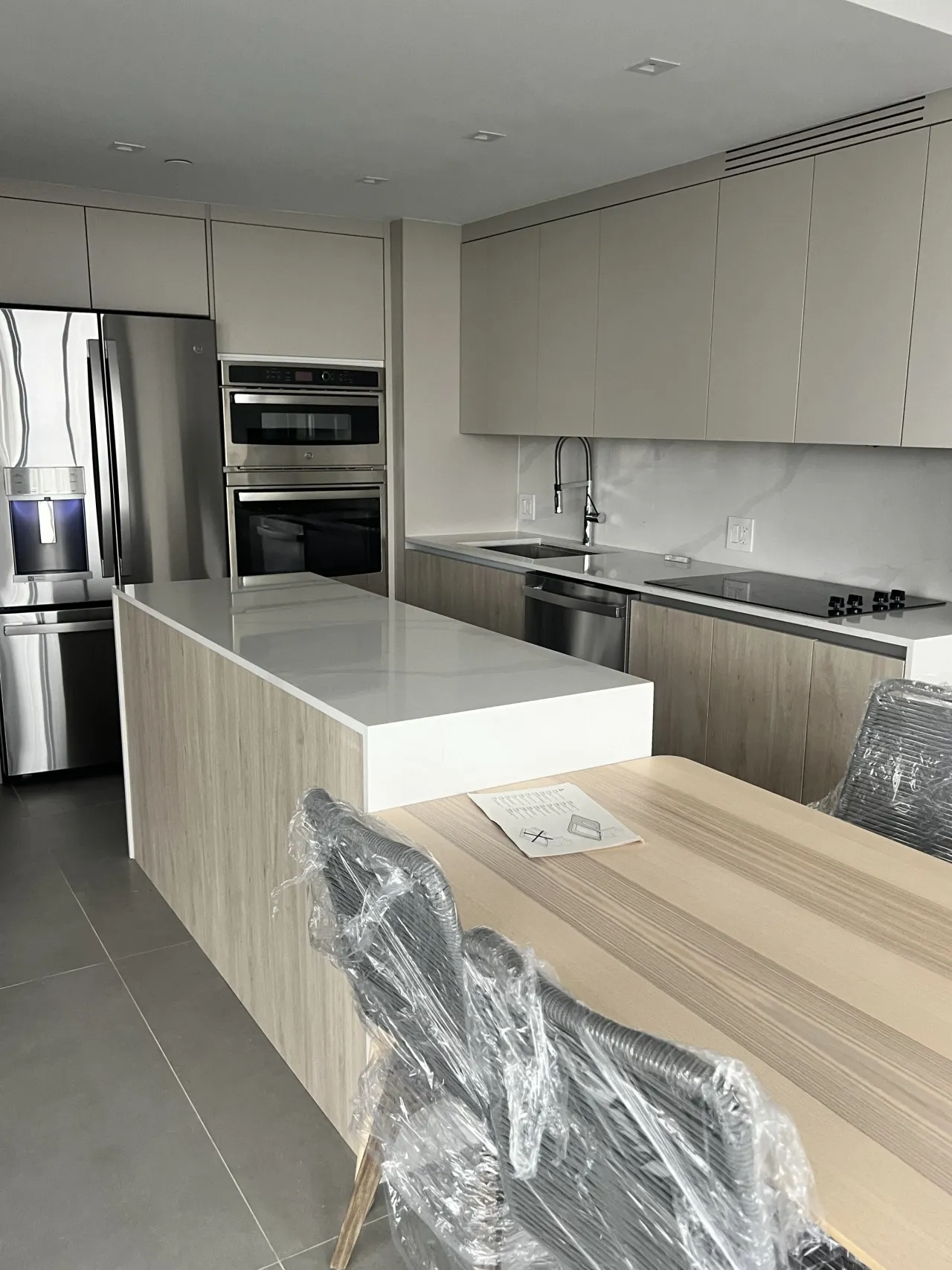 Light gray/taupe kitchen with a stainless French-door refrigerator, a wall oven column, and a white stone island with a dining table extension