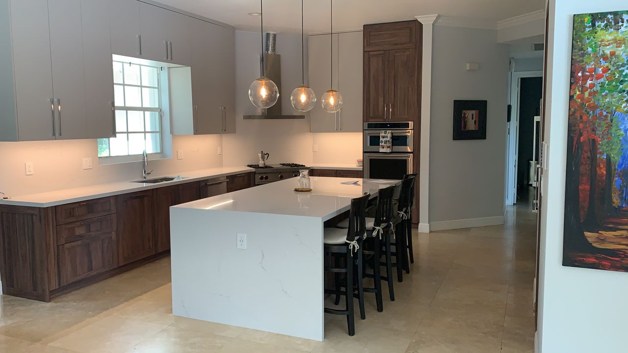 Kitchen with light gray upper cabinets, dark wood-grain base cabinets, a white stone waterfall island, and three clear glass globe pendants