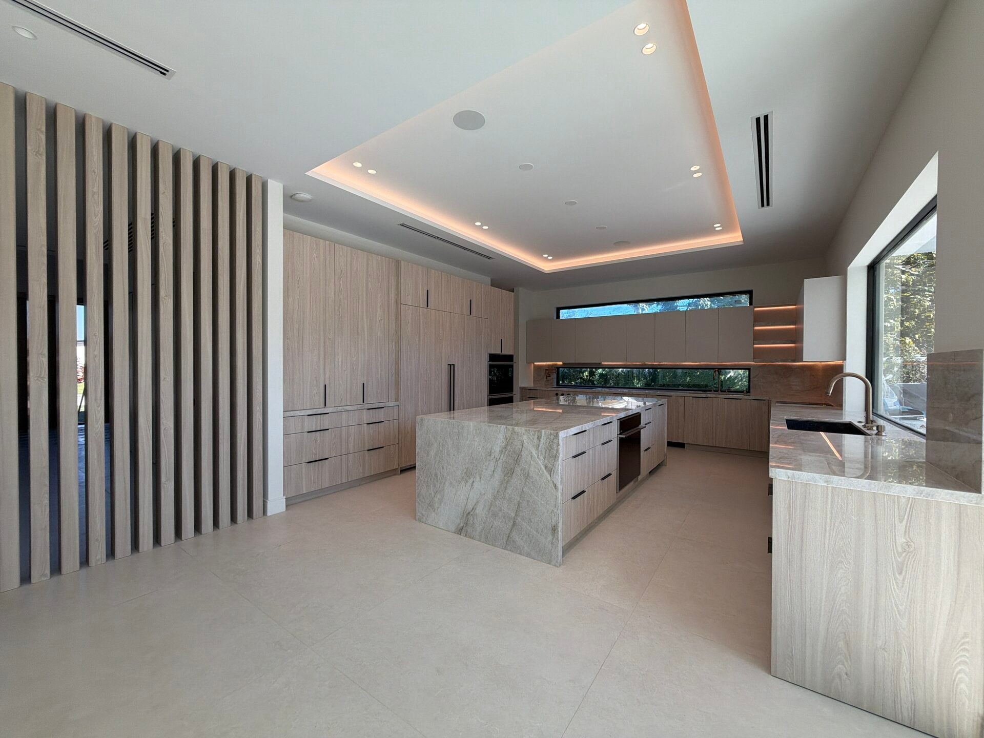 Modern kitchen with light wood cabinetry, a gray-veined stone waterfall island, black bar-style hardware, and a vertical wood-slat accent wall