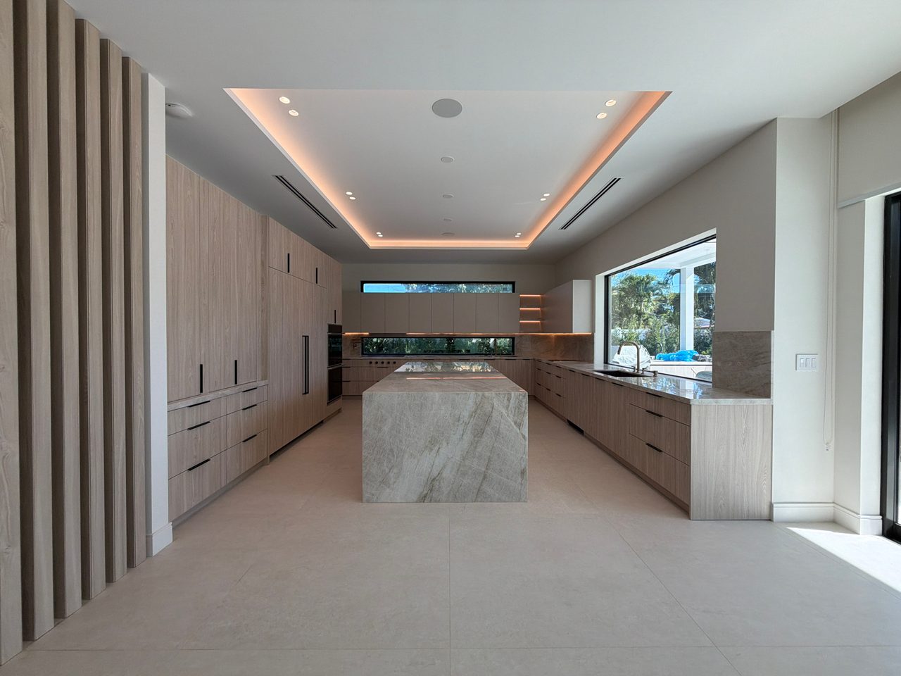 Light wood-grain melamine kitchen with a veined-stone waterfall island, matching perimeter counters, and narrow horizontal windows above the backsplash