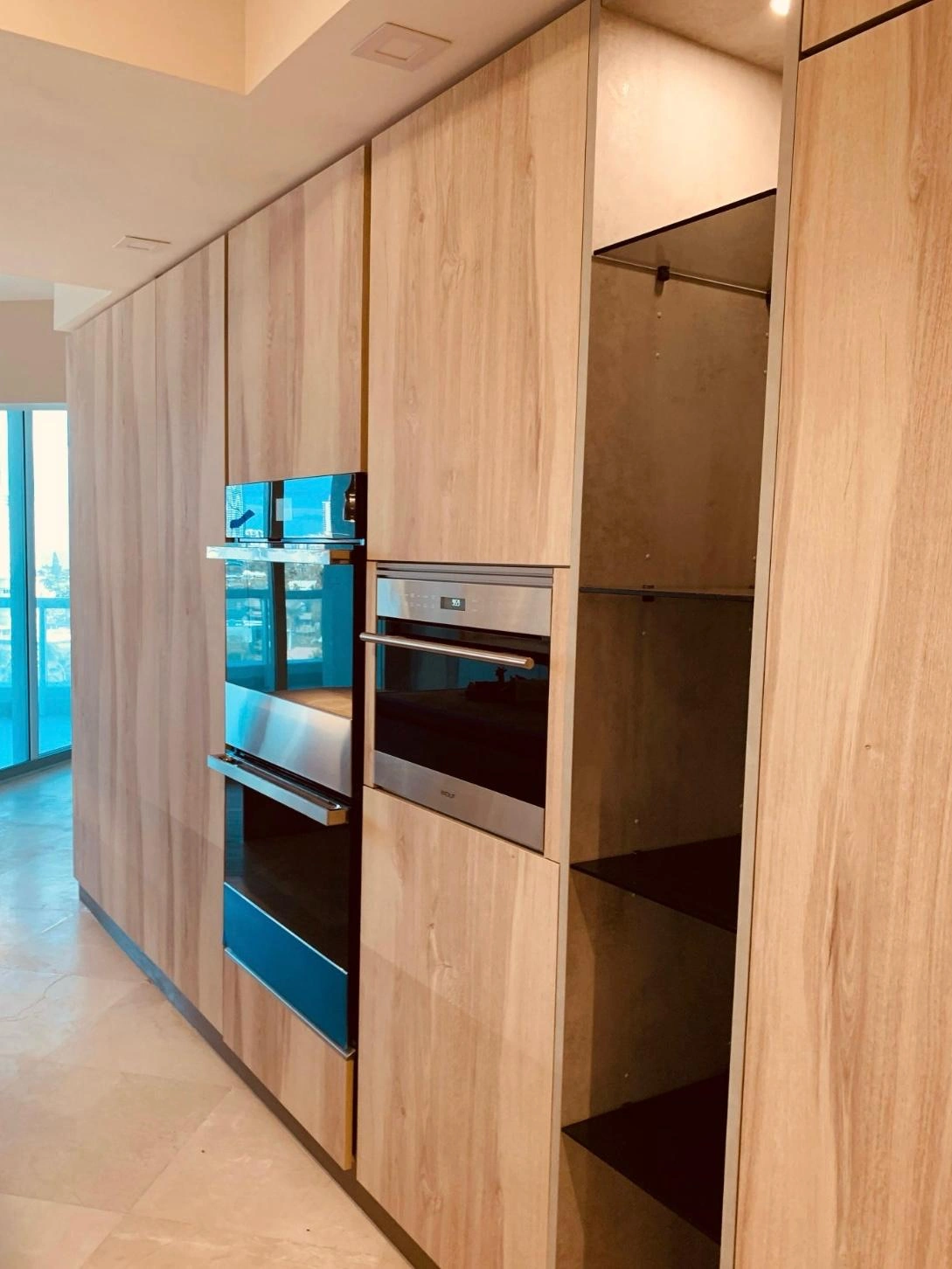 Light wood tall cabinet wall with wall ovens and reflective glass panel doors