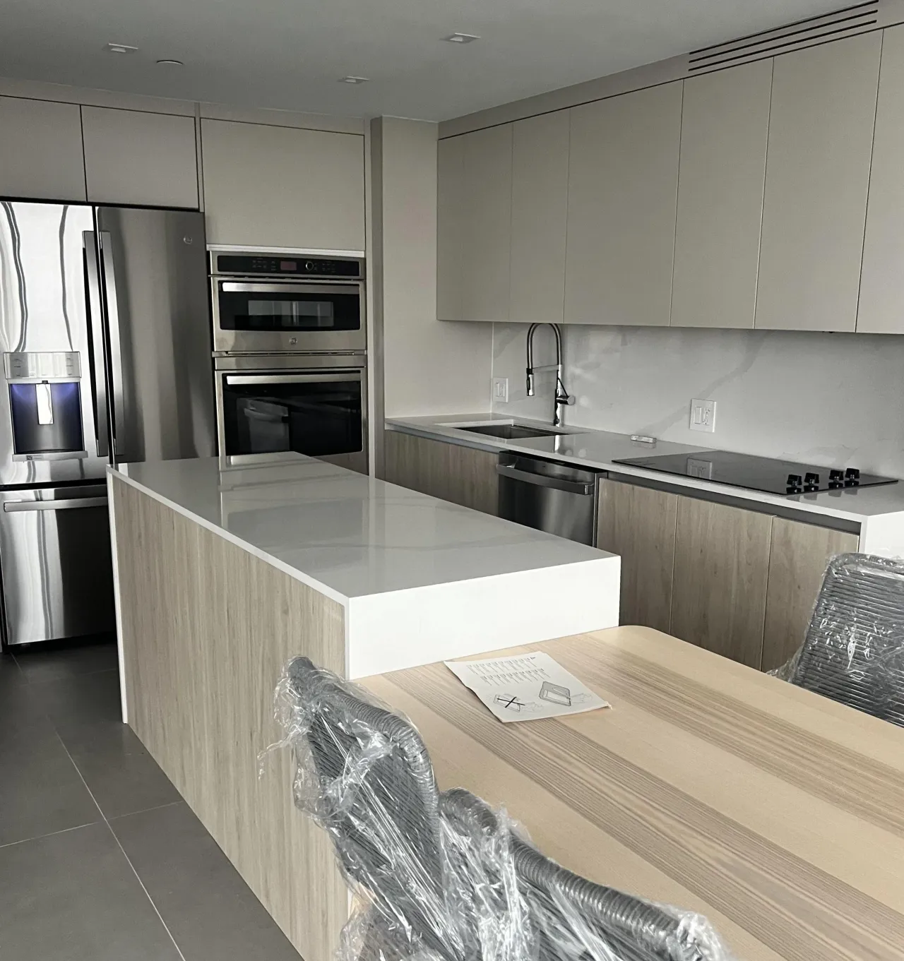 Light wood and taupe kitchen with a stainless French-door fridge, a wall oven column, and a white stone island countertop