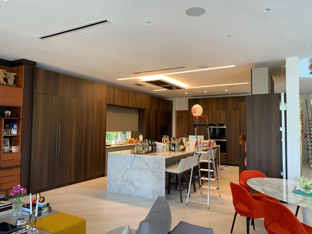 Open-plan kitchen with a large veined-stone waterfall island, floor-to-ceiling dark wood-grain cabinetry, and an adjoining living and dining area