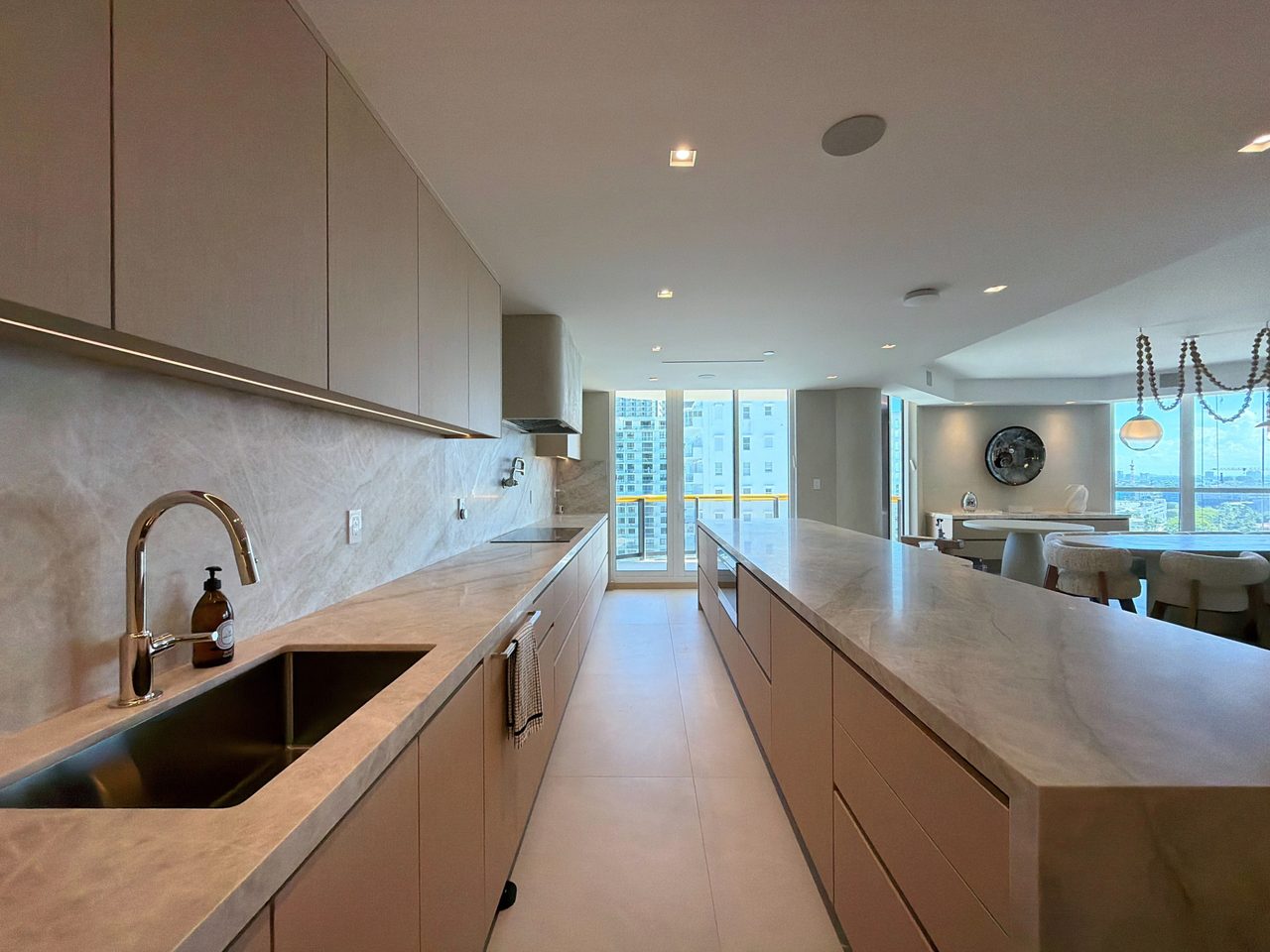 Pale wood veneer galley run with a veined-stone counter and slab backsplash, an undermount sink, an induction cooktop, and a city-view window