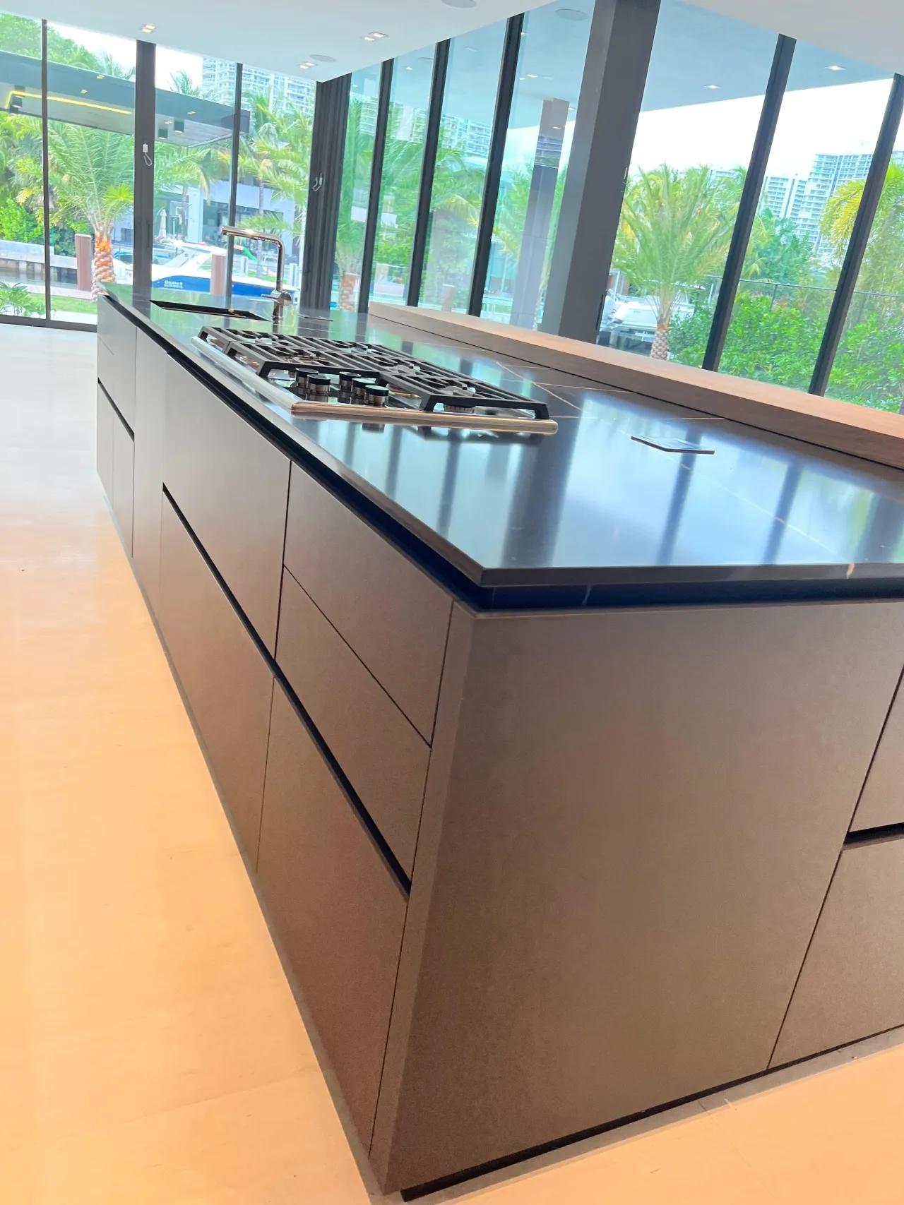 Sleek black kitchen island with a stainless gas cooktop set in a dark stone counter, floor-to-ceiling windows with a city view