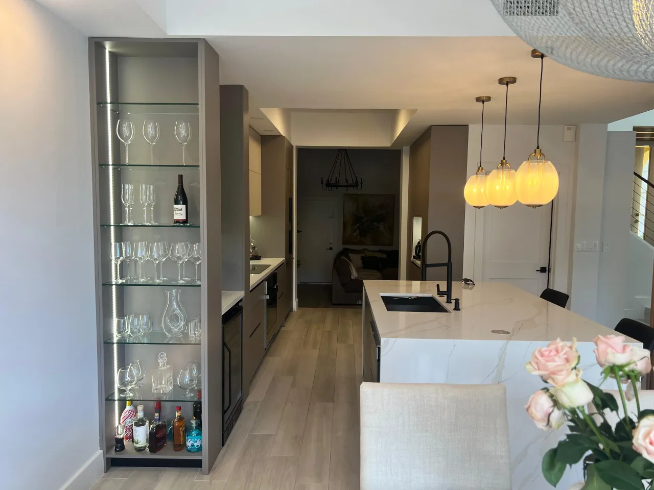 Taupe kitchen with glass wine display shelving holding bottles and glasses, a veined-stone island, and globe pendant lights