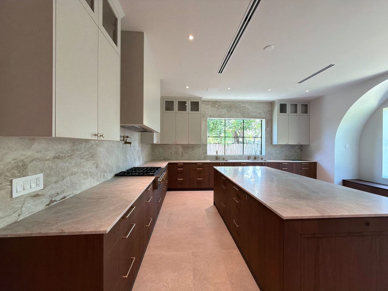 Two-tone melamine kitchen with dark wood-grain base cabinets, cream uppers and hood, veined-stone slab counters and backsplash, and two islands