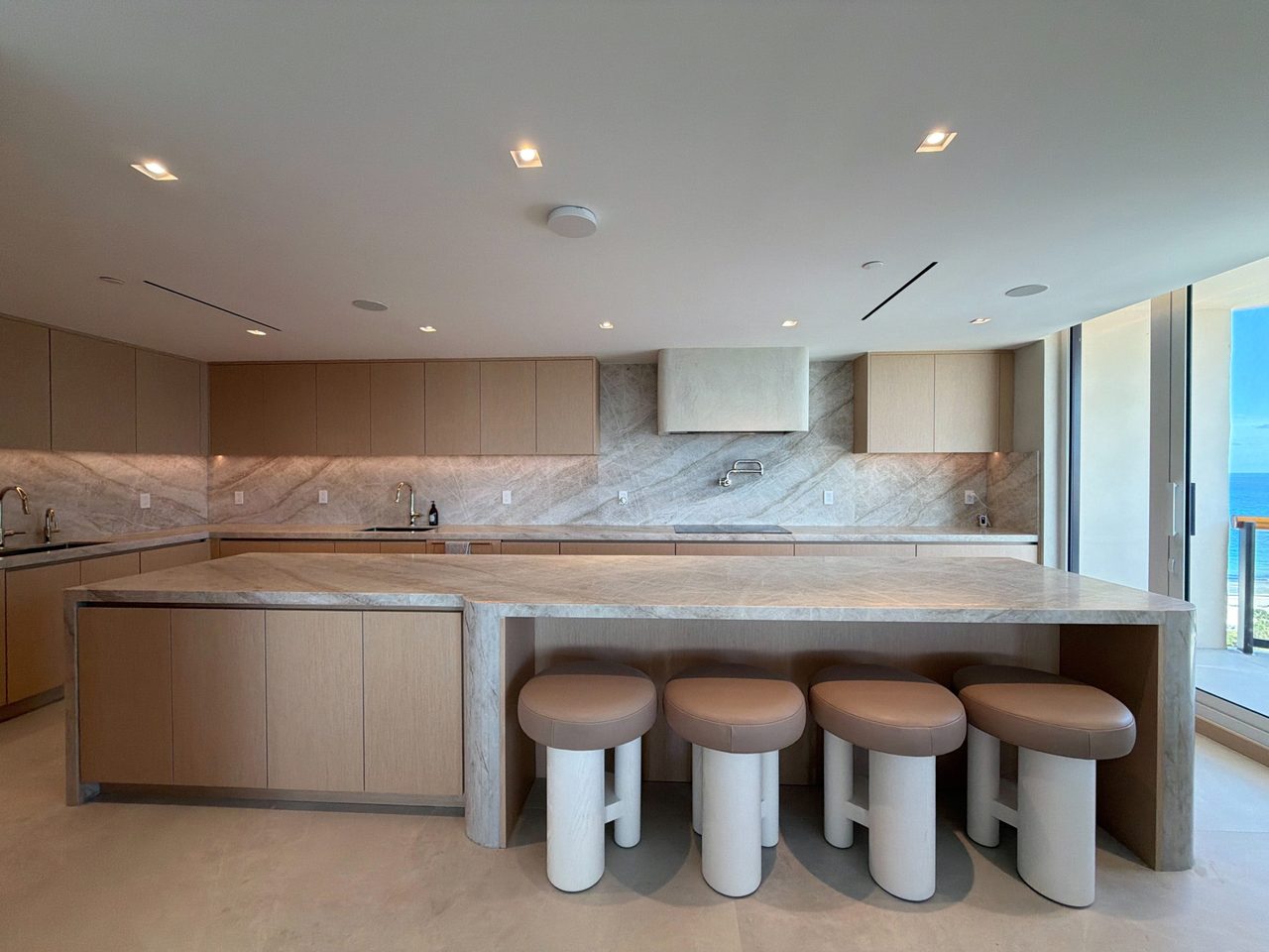 Veined-stone waterfall island with four round leather-topped stools and a stone-wrapped hood centered on a full slab backsplash