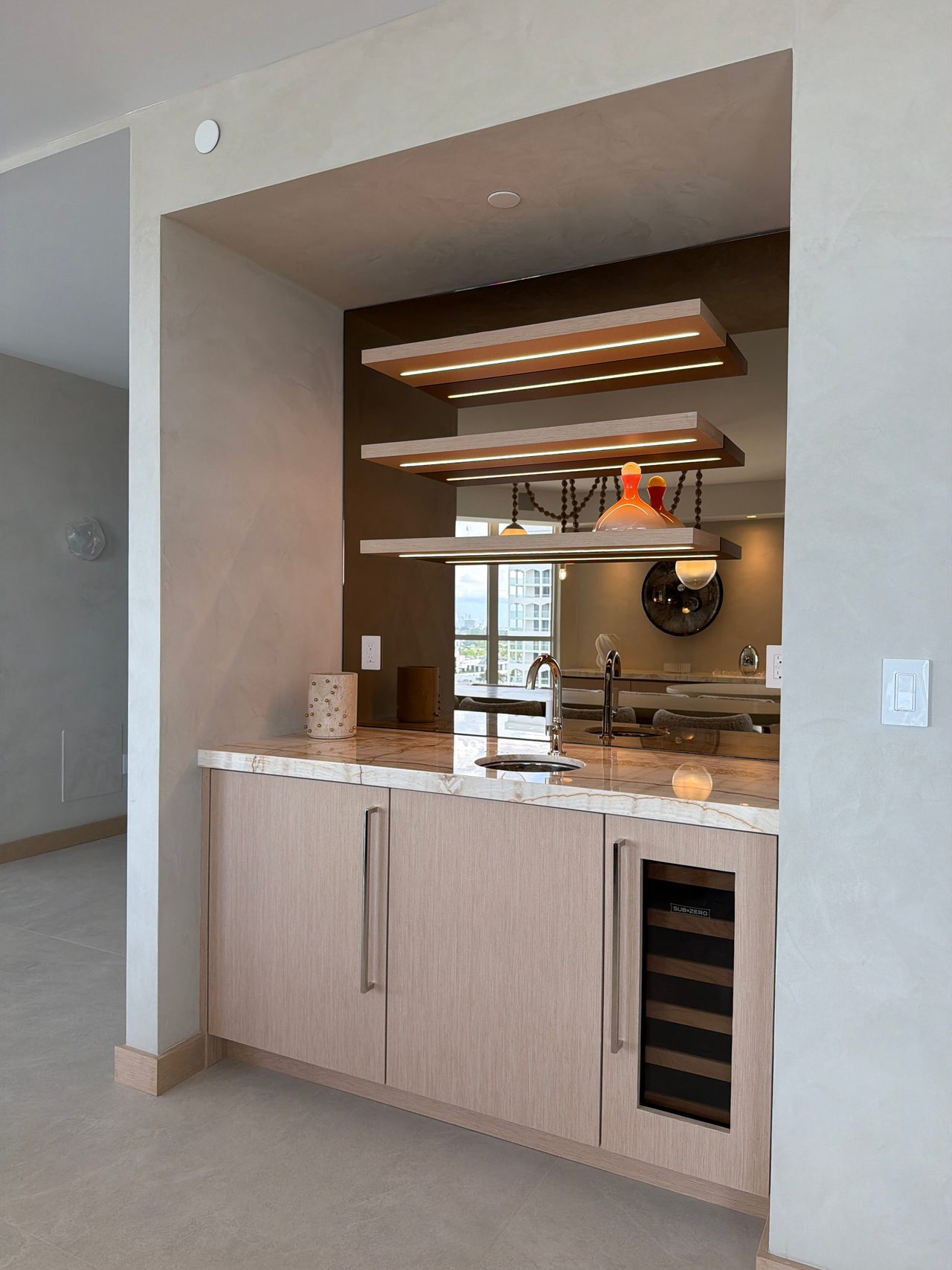Custom-stained wood veneer wet bar with three floating shelves lit by integrated LEDs, a bronze mirror back panel, and a glass-front wine refrigerator