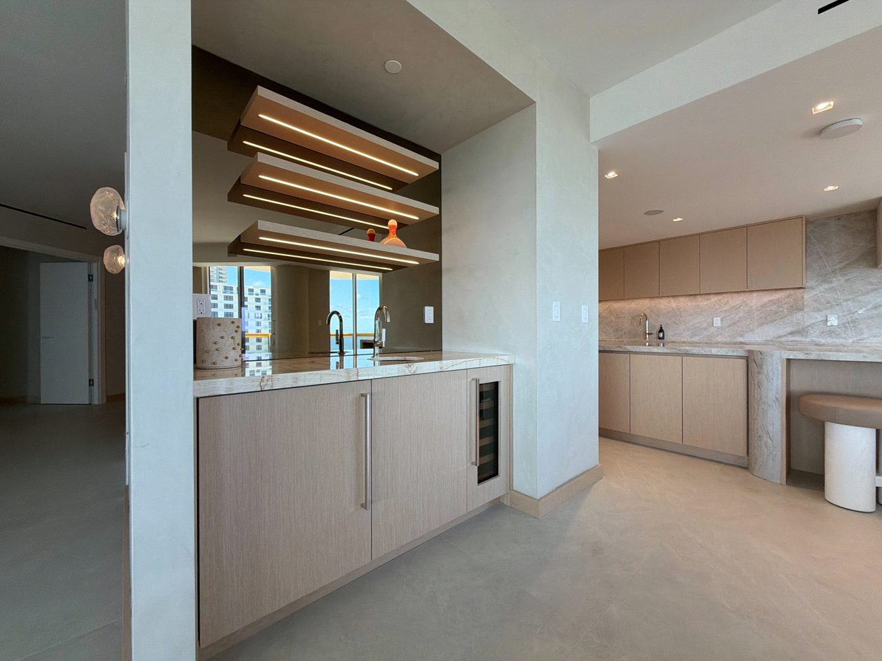 Custom-stained wood veneer wet bar with integrated-LED floating shelves and a bronze mirror back, opening to a second wet bar and dining area beyond