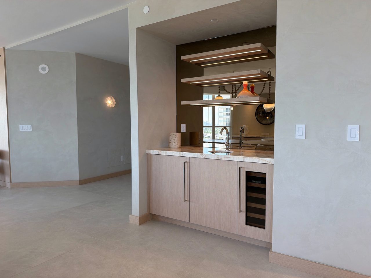 Custom-stained wood veneer wet bar in an arched pass-through, with three integrated-LED floating shelves, a bronze mirror back, and a wine refrigerator