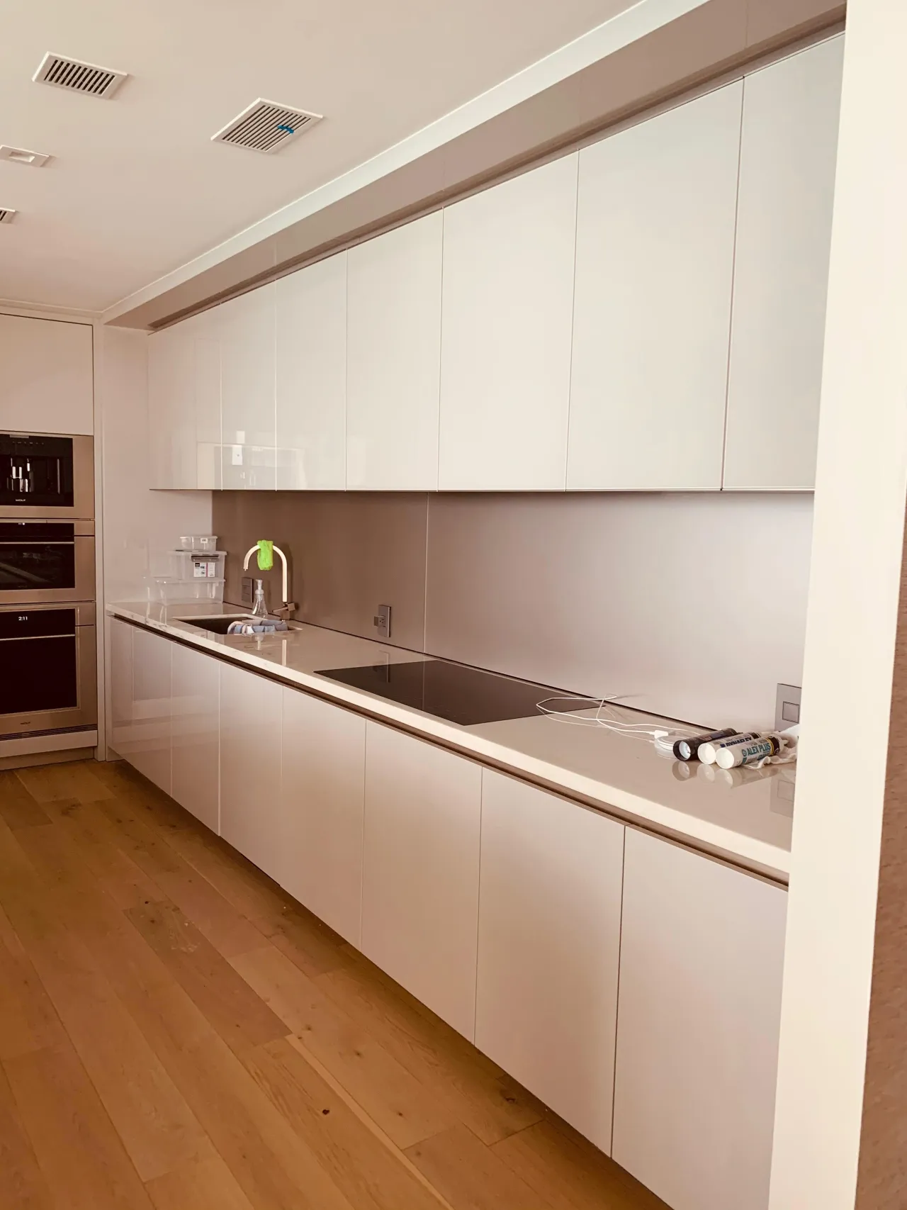 White handleless kitchen cabinets along a long galley wall with a black induction cooktop set in a light counter and a wood floor