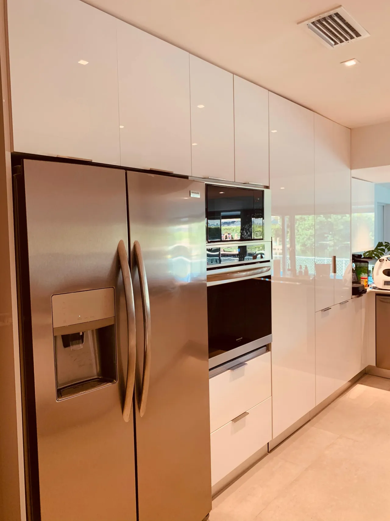 White high-gloss floor-to-ceiling cabinets with an integrated stainless fridge and a built-in wall oven/microwave column