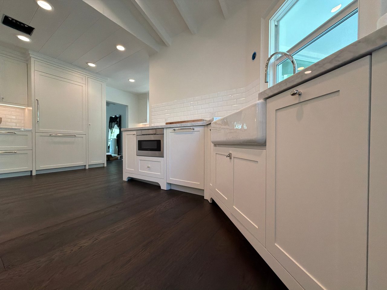 Apron sink and panel-front dishwasher in white shaker cabinetry with stone-look counters, a microwave drawer, and a paneled refrigerator behind